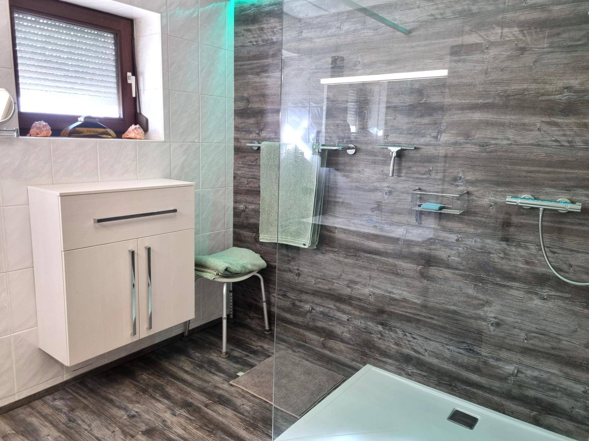Modernes Badezimmer mit begehbarer Dusche, Holzoptik-Fliesen und Fenster für angenehmes Tageslicht.