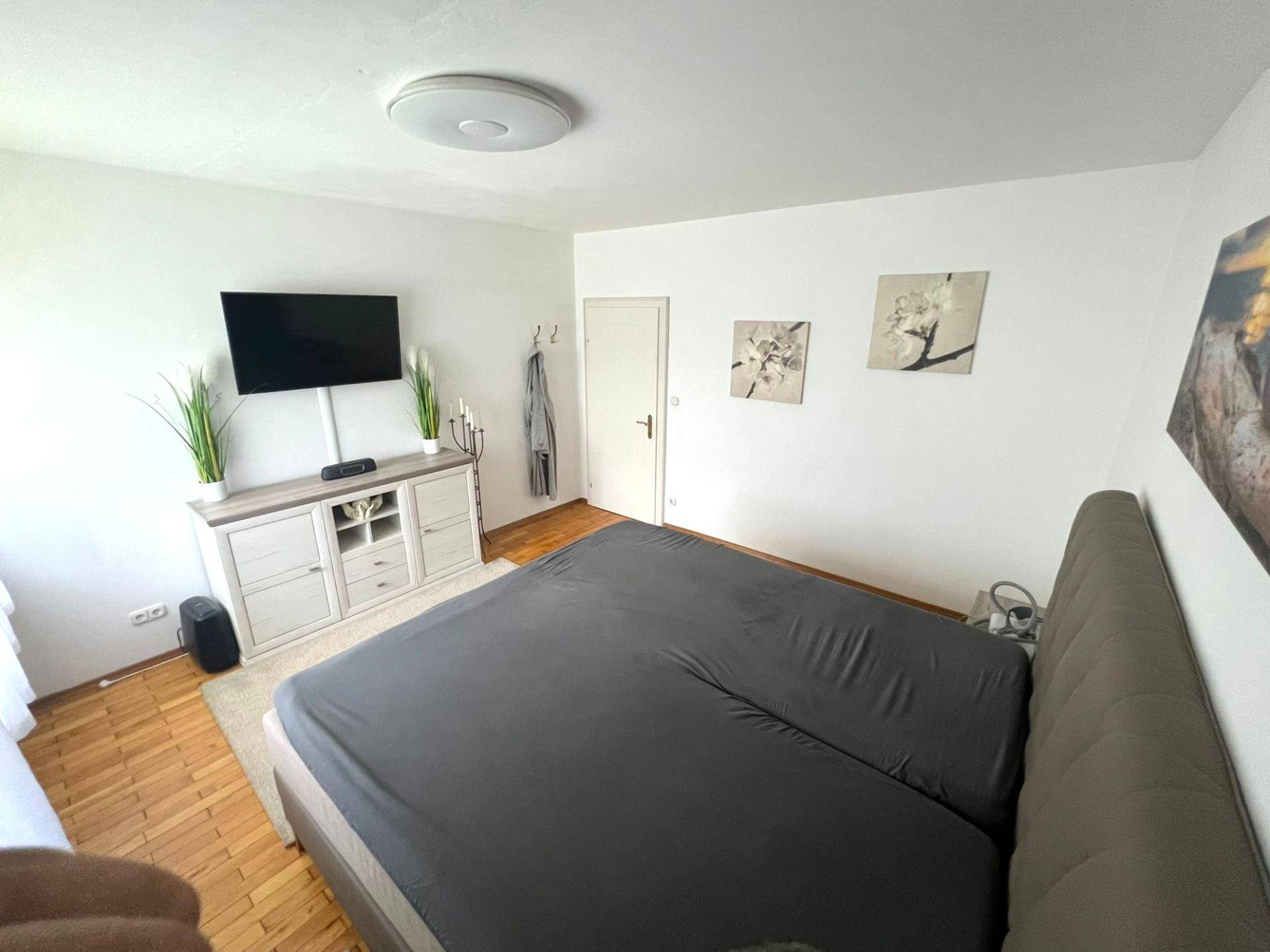 Helles Schlafzimmer mit Doppelbett, Holzfußboden und schlichter, moderner Einrichtung für erholsame Nächte.