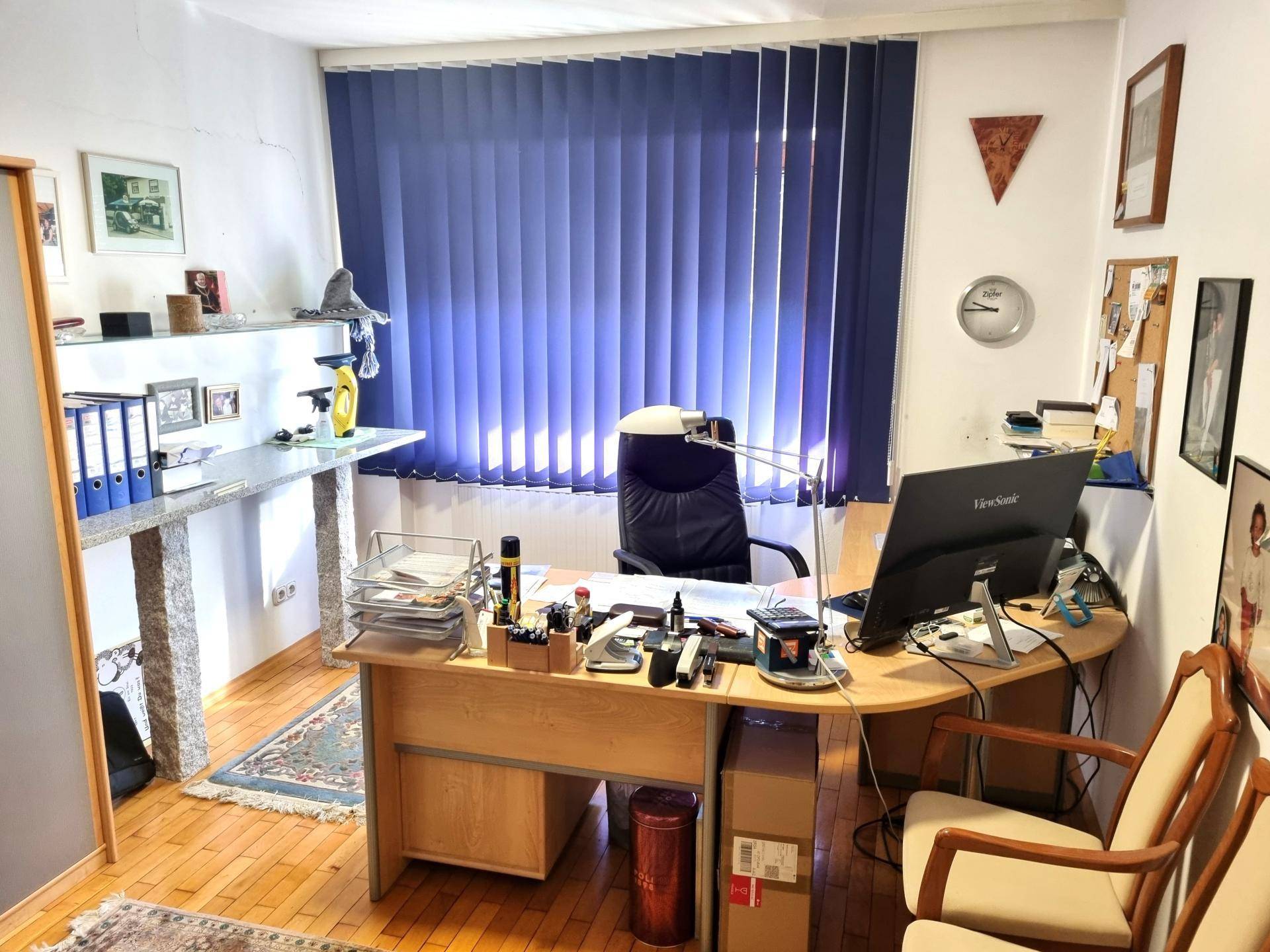 Funktionales Büro mit Schreibtisch, Bürostuhl und großem Fenster mit Jalousien für konzentriertes Arbeiten.