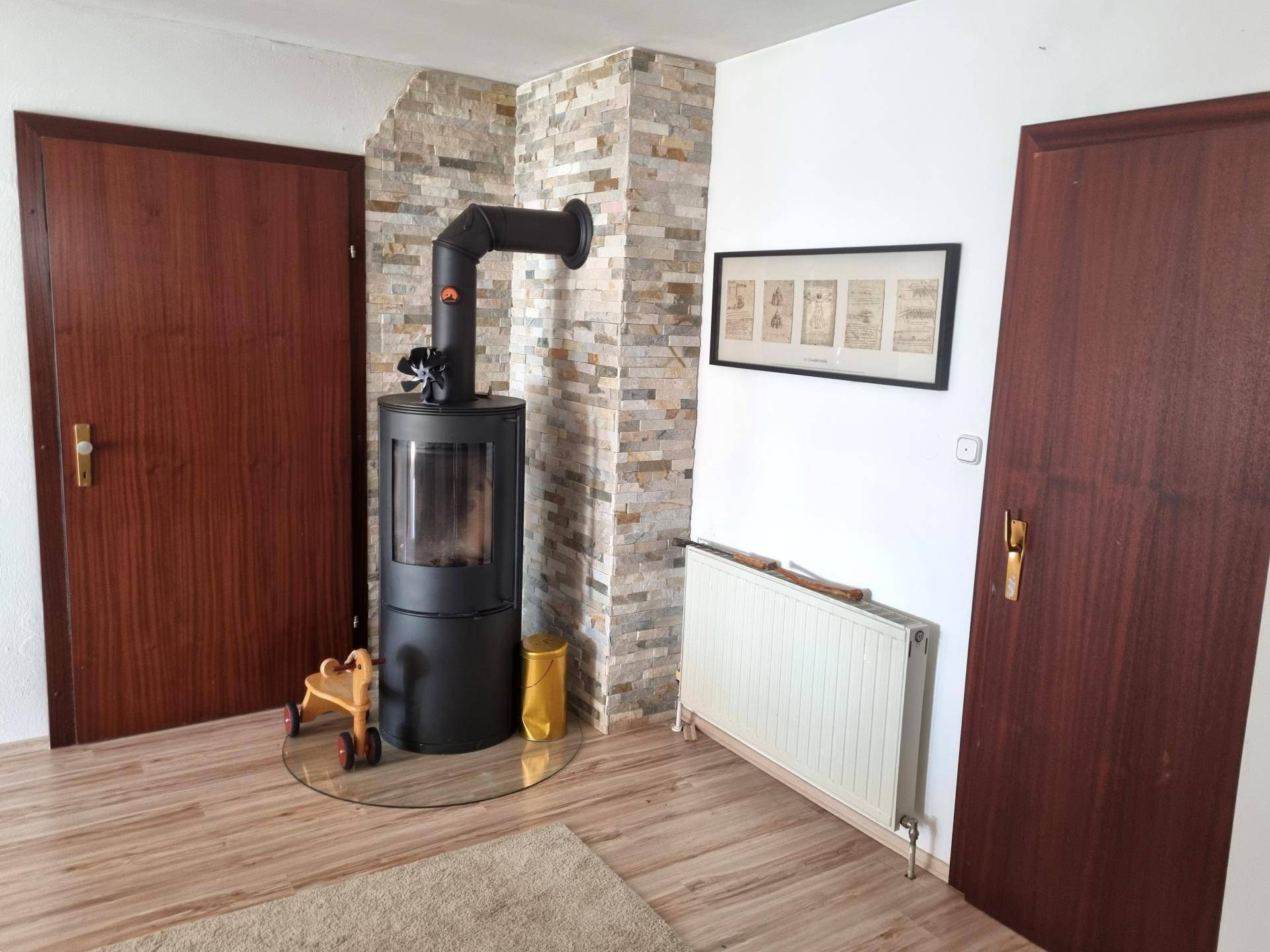 Gemütlicher Raum mit modernem Holzofen, Steinwand und Holzfußboden, ideal für kalte Tage.