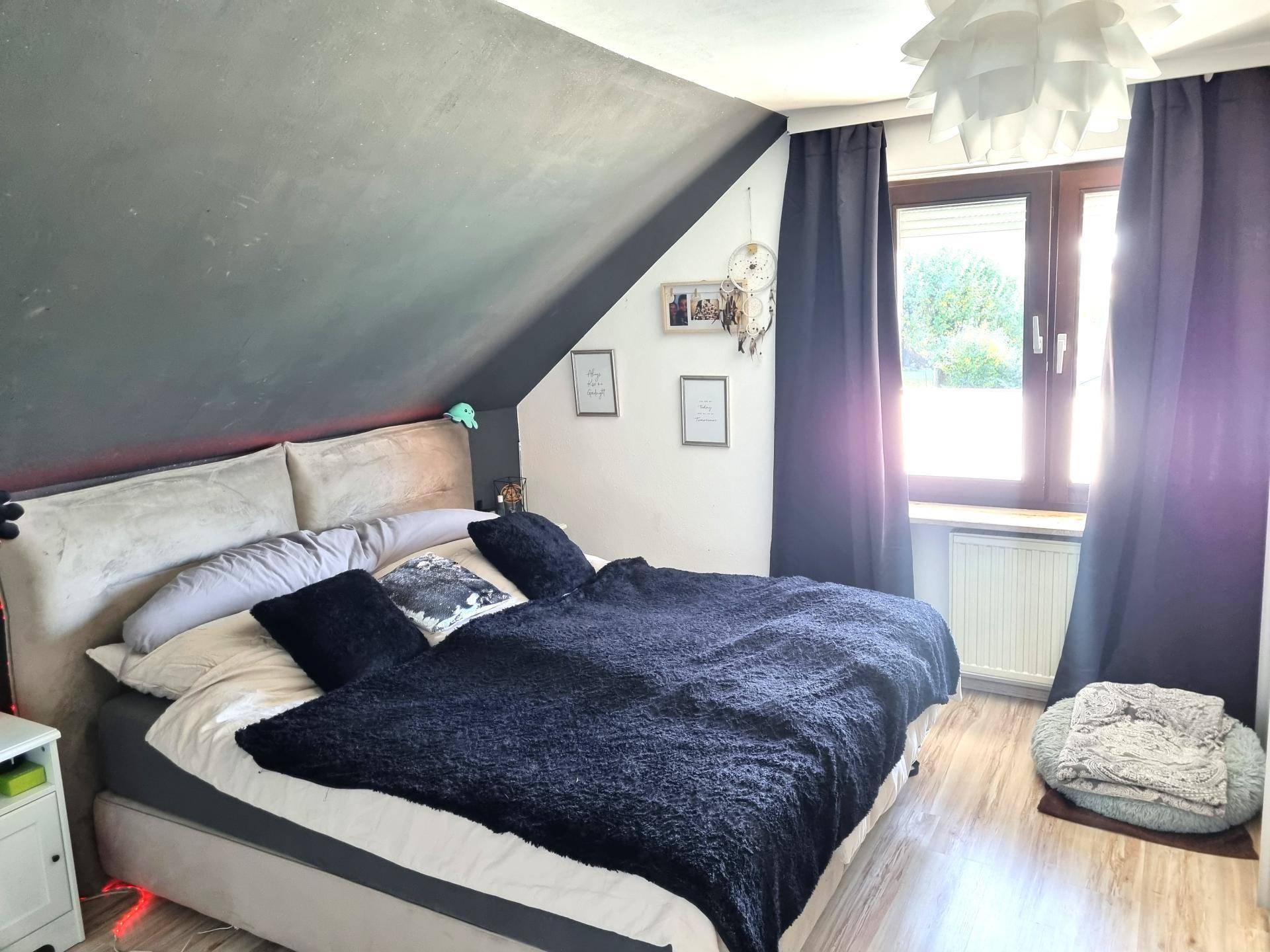 Gemütliches Schlafzimmer im Dachgeschoss mit Dachschräge, Doppelbett und Fenster für viel Tageslicht.