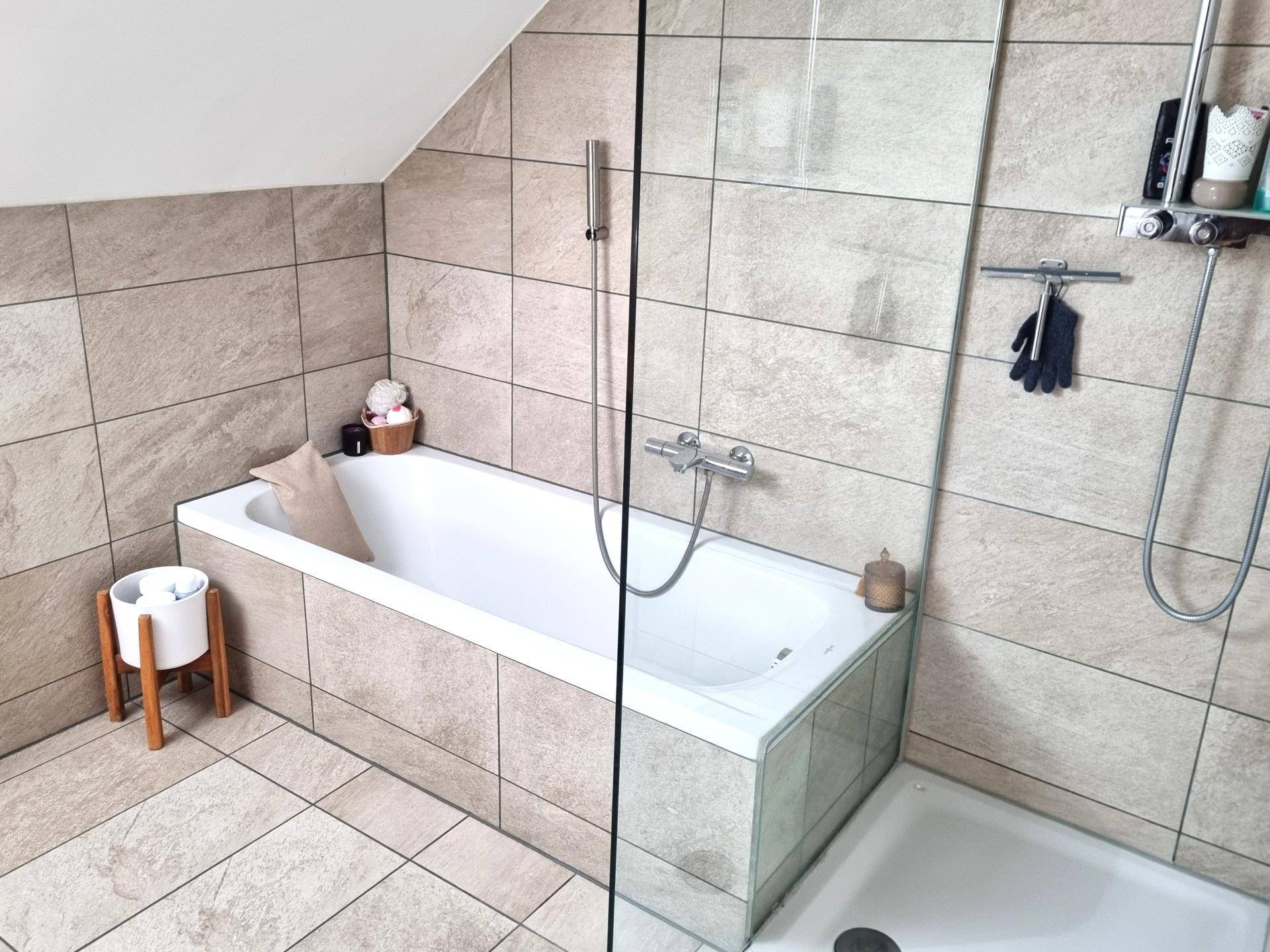 Badezimmer mit Badewanne, Duschbereich und Fliesen in Natursteinoptik, funktional und gepflegt.