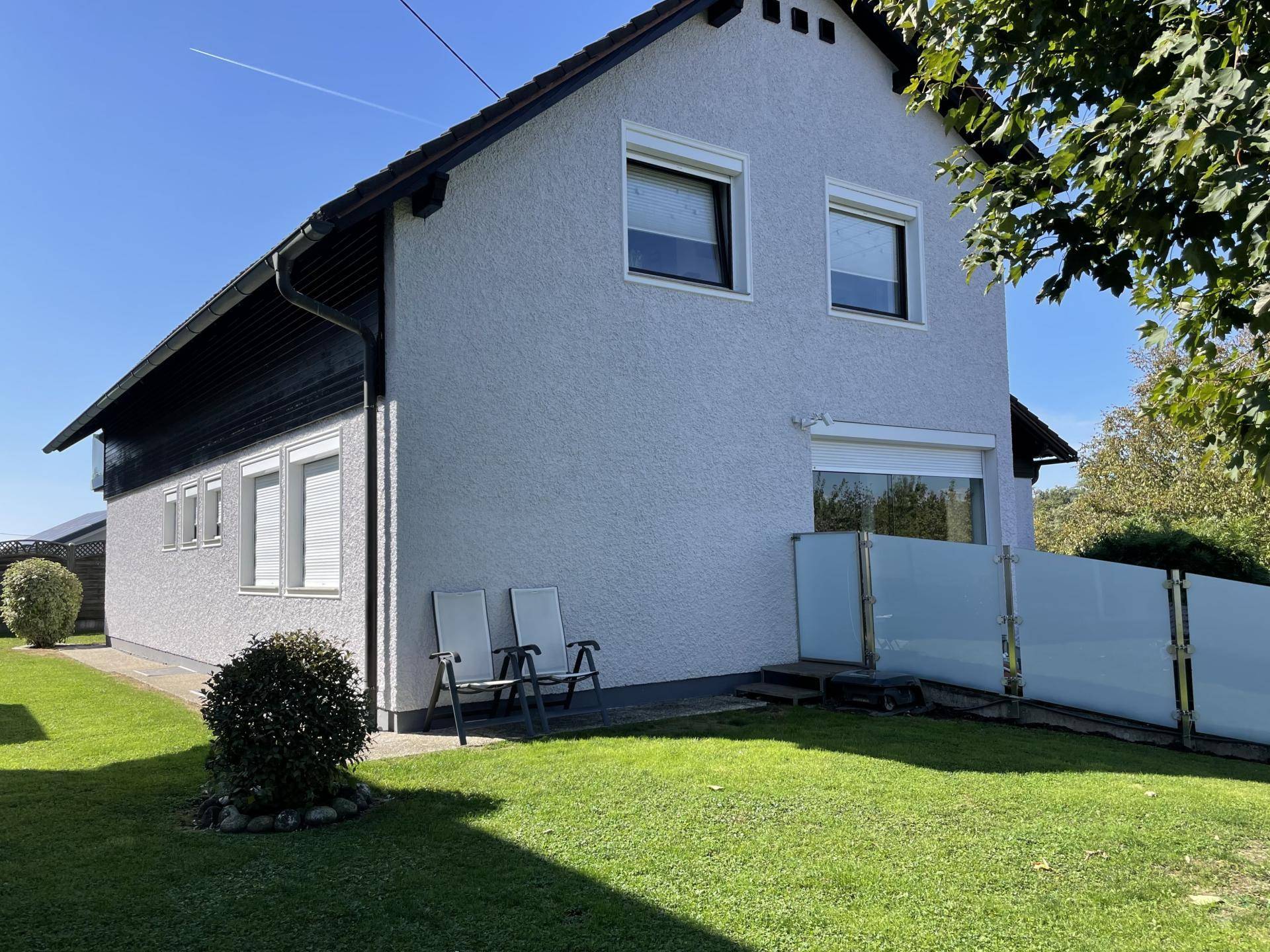 Seitenansicht des Hauses mit gepflegtem Rasen und Sitzgelegenheiten im Garten an einem sonnigen Tag.