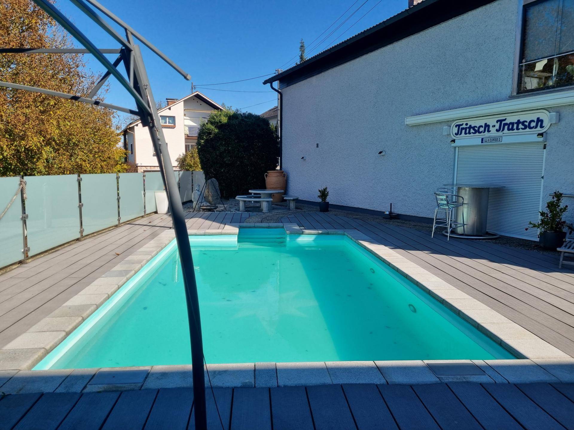 Außenpool mit Holzdeck und angrenzendem Gebäude unter blauem Himmel, ideal für heiße Tage.