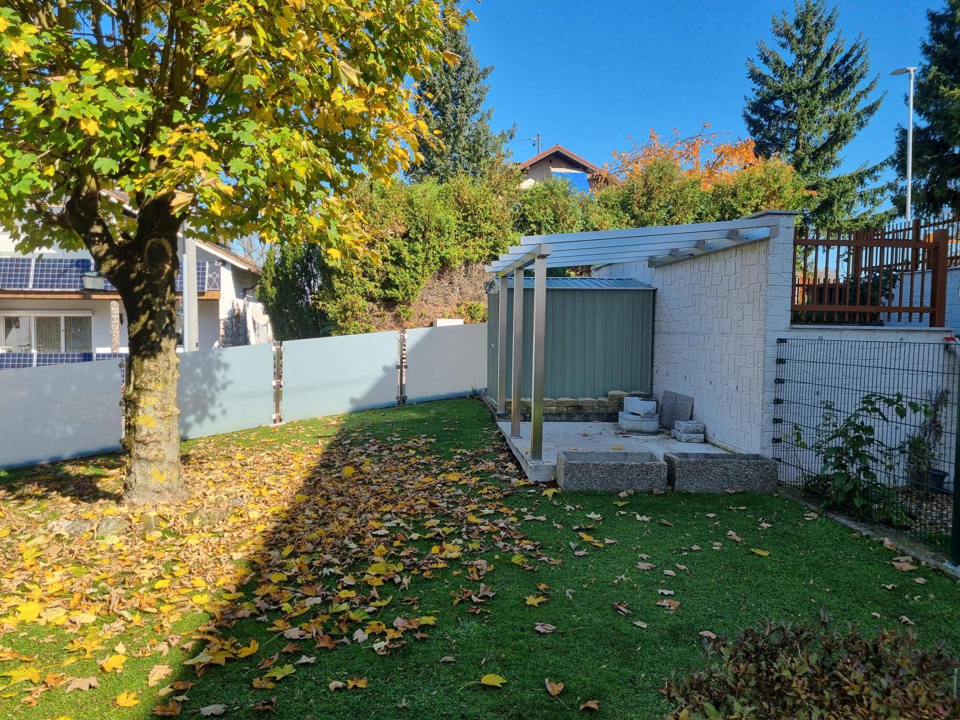 Gepflegter Garten mit Rasenfläche, Herbstlaub und einem kleinen Geräteschuppen an einem sonnigen Tag.