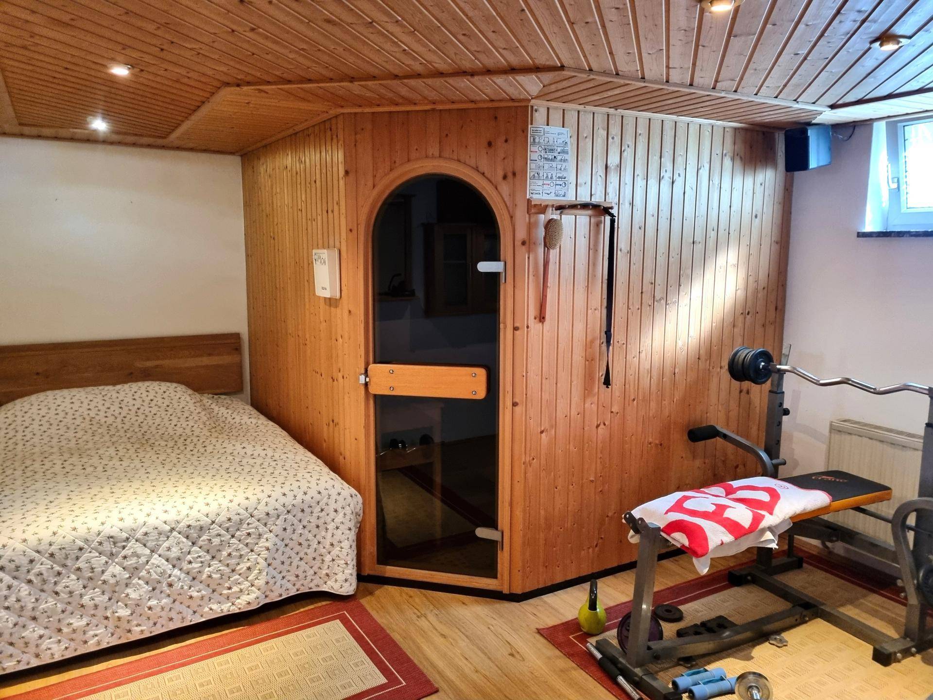 Wellnessbereich mit Sauna, Fitnessgeräten und einem Bett, ideal zur Entspannung und sportlichen Betätigung.