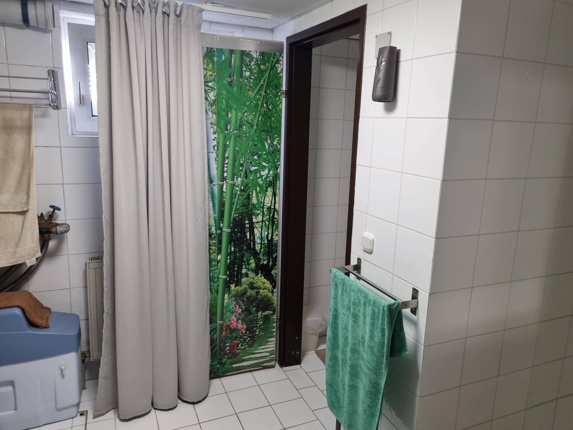 Einfaches Badezimmer mit Duschbereich, Fliesen und Fenster, funktional und hell gestaltet.