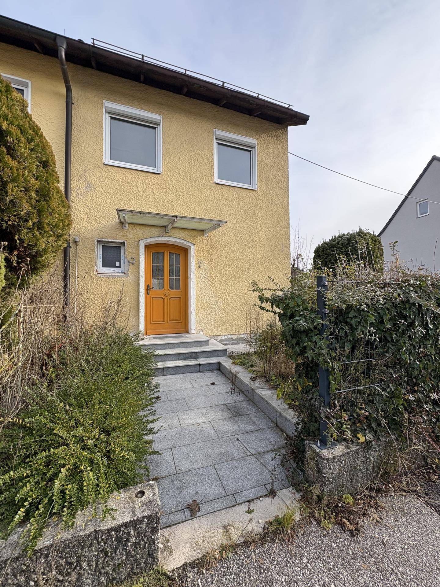 Vorderansicht des Hauses mit gelber Fassade, Eingangstür und einem gepflasterten Zugangsweg.