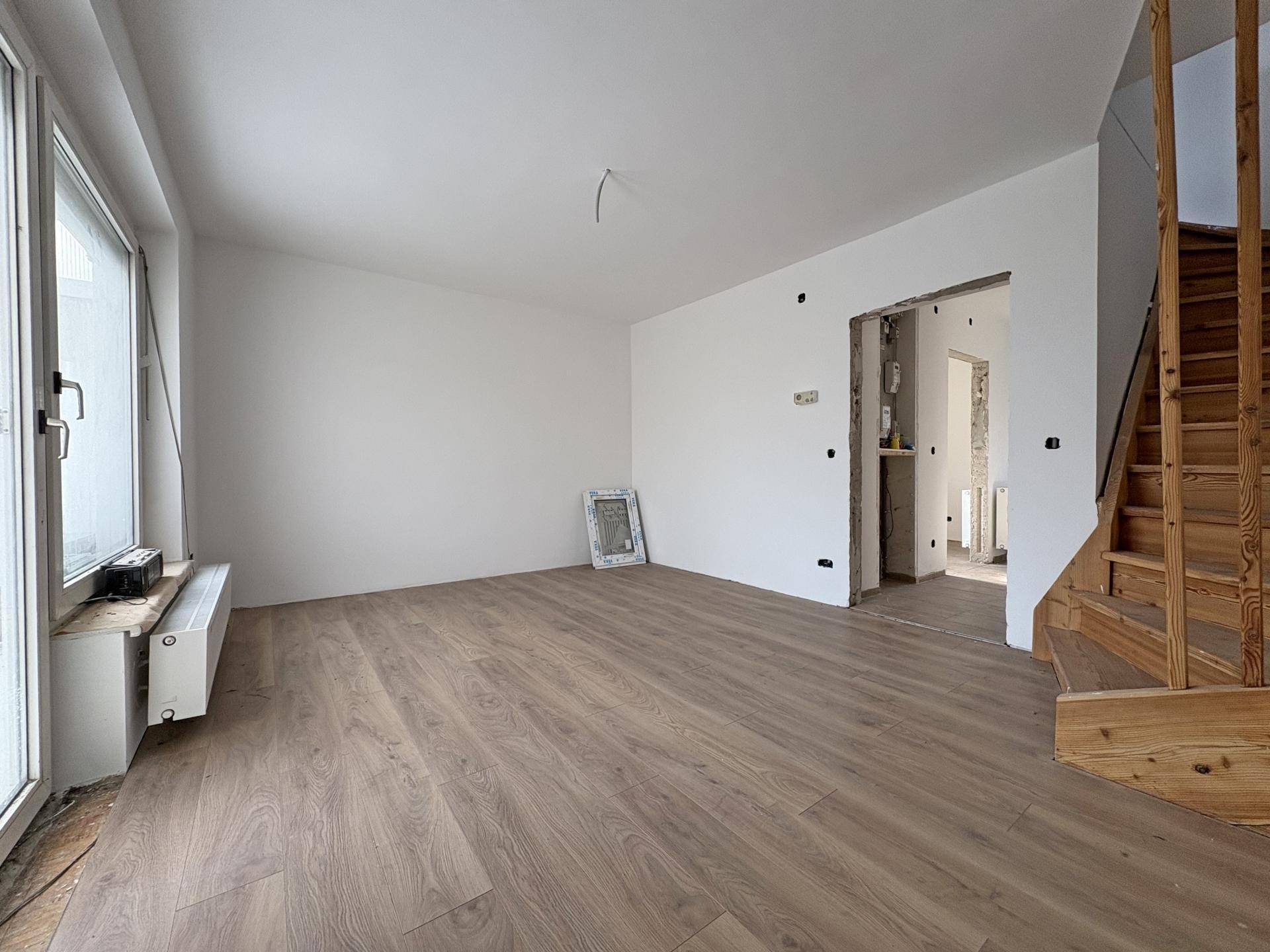 Leerer Raum mit Laminatboden, Holztreppe und offenem Durchgang zu weiteren Bereichen.