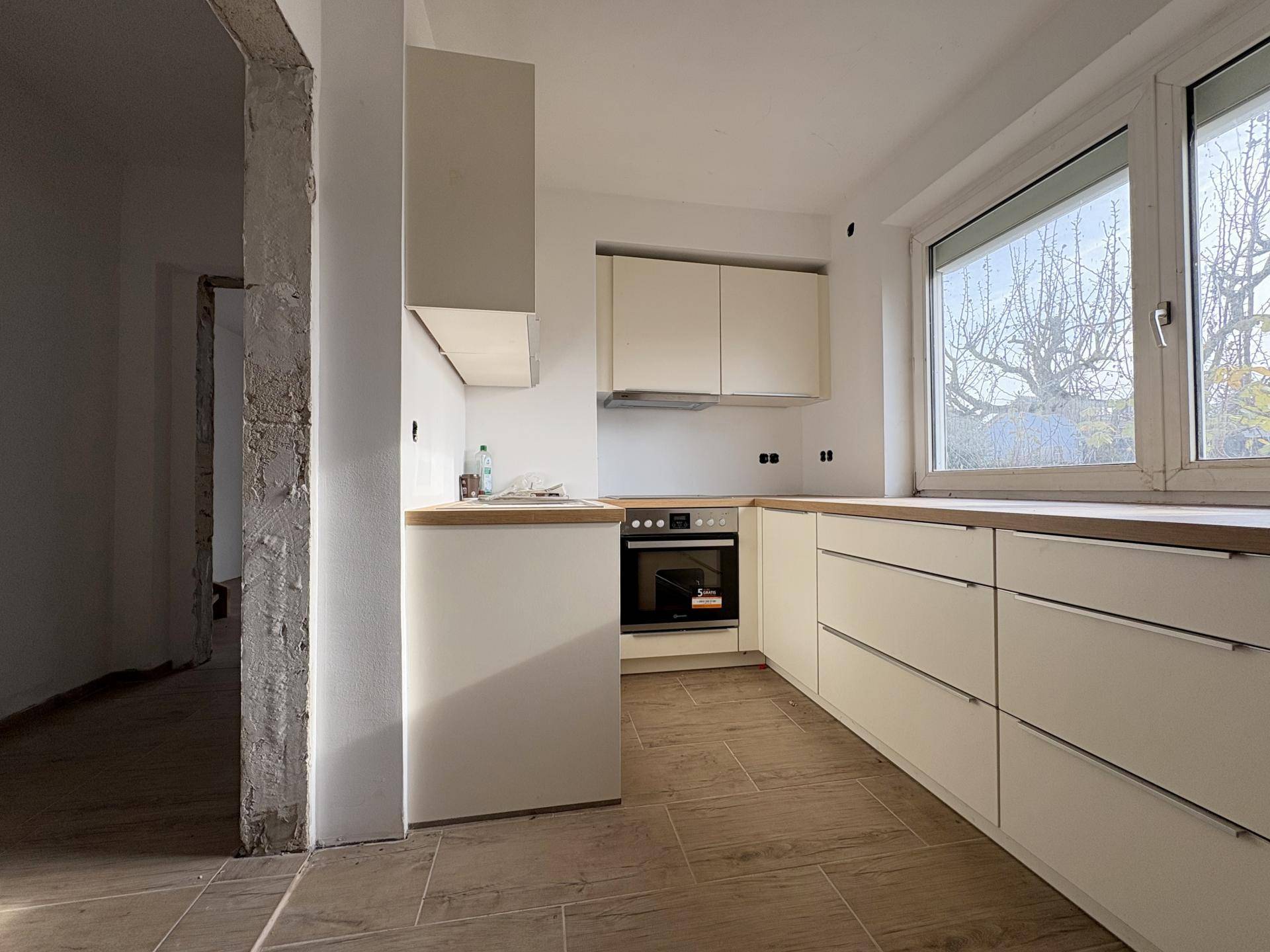 Küche im Rohbauzustand mit neuen Unterschränken, Holzarbeitsplatten und Fenster.