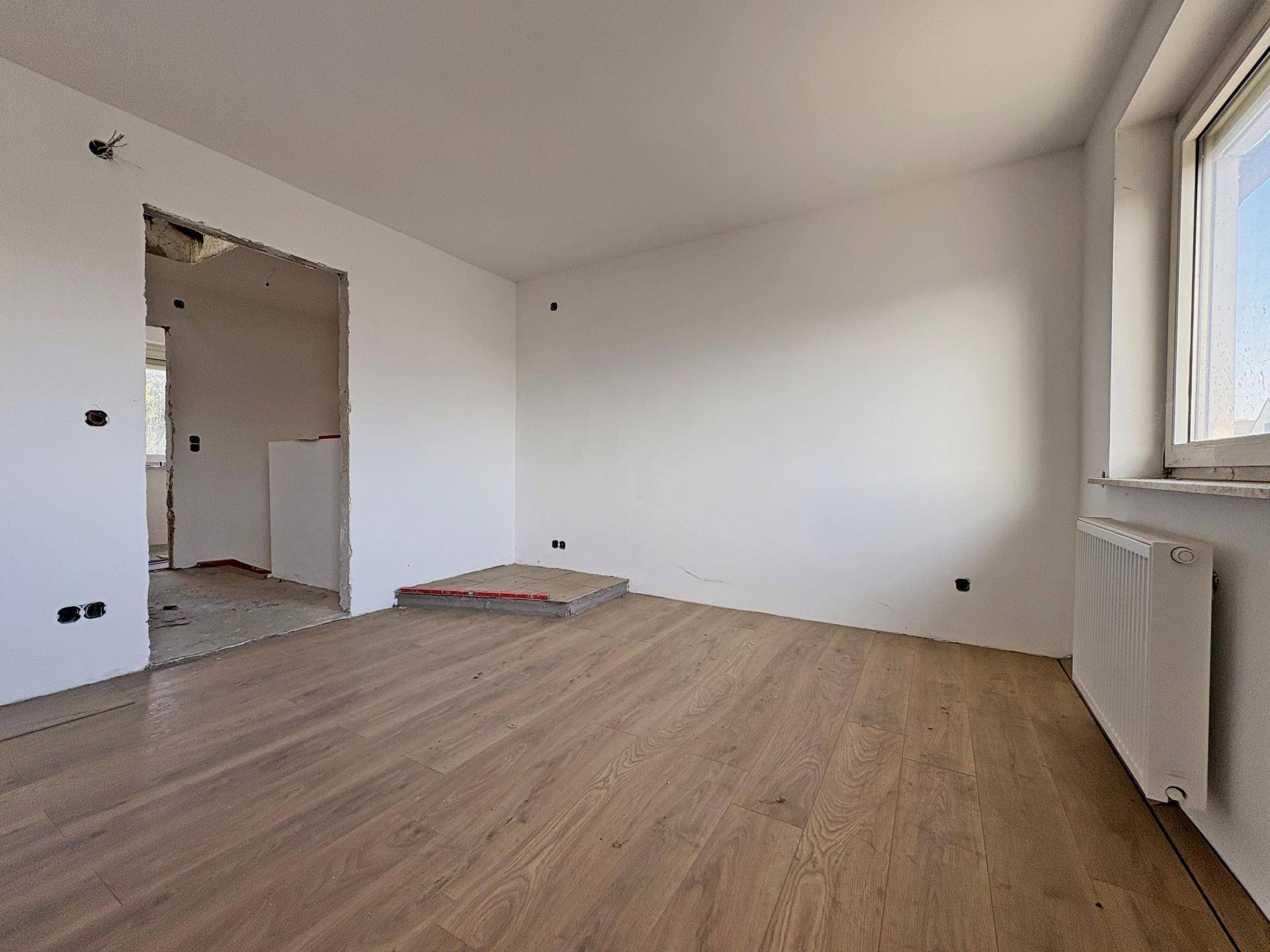 Leerer Raum mit Laminatboden, Fenster und Heizkörper, der auf die Renovierung wartet.