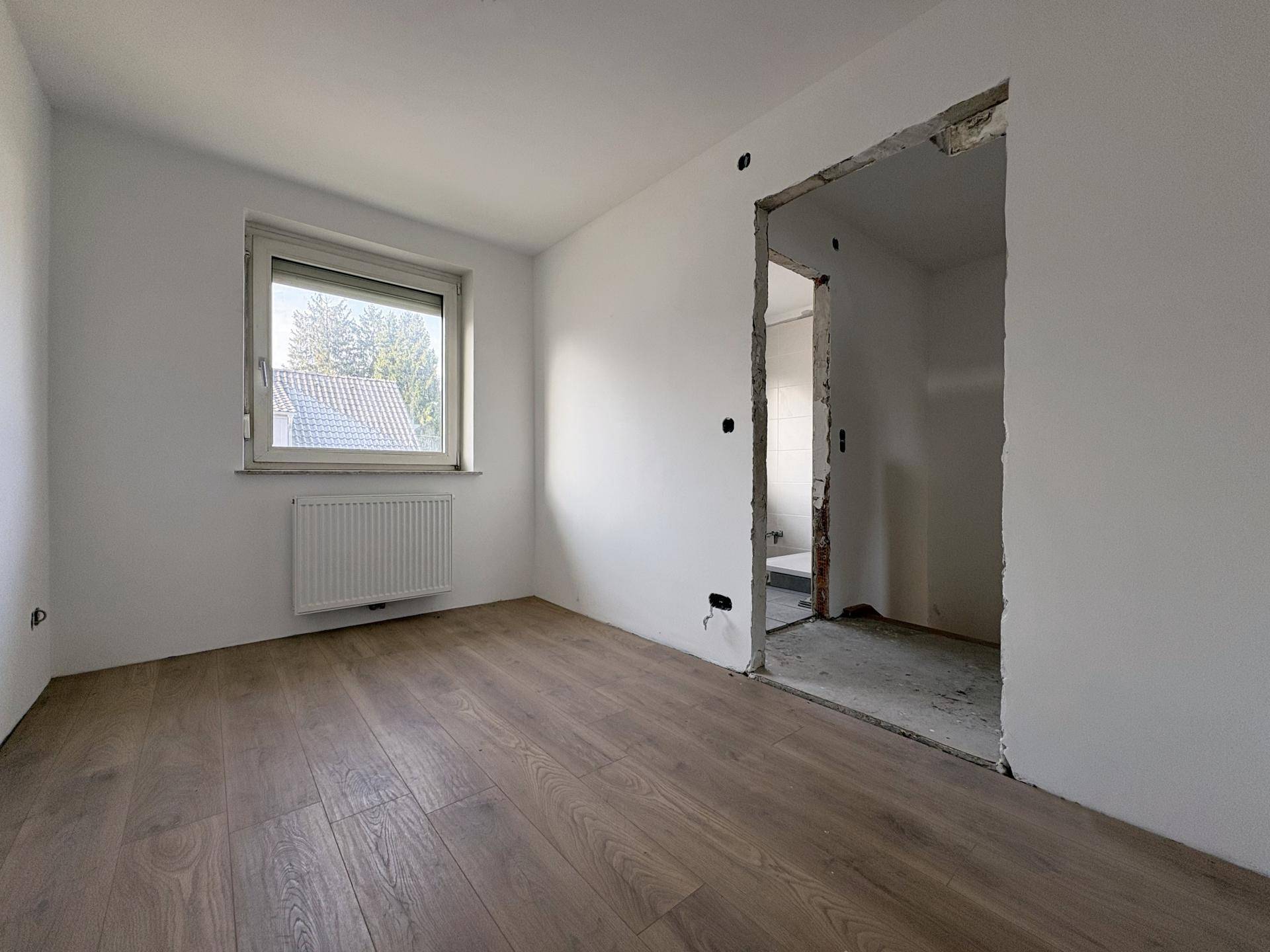 Leerer Raum mit Laminatboden, Fenster und Heizkörper, der auf die Fertigstellung wartet.