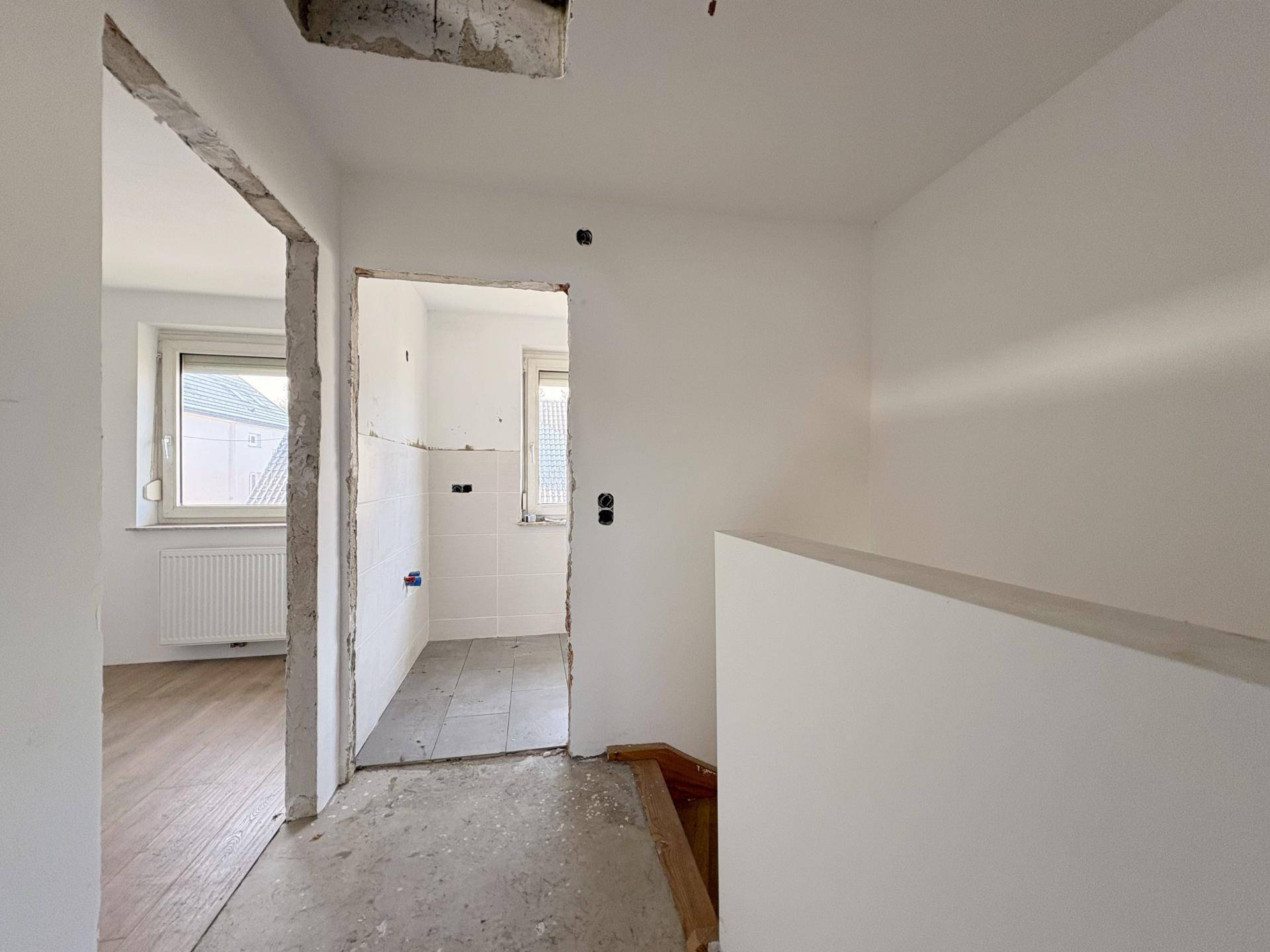 Flur im Rohbauzustand mit Zugang zu einem Badezimmer, das ebenfalls renoviert wird.