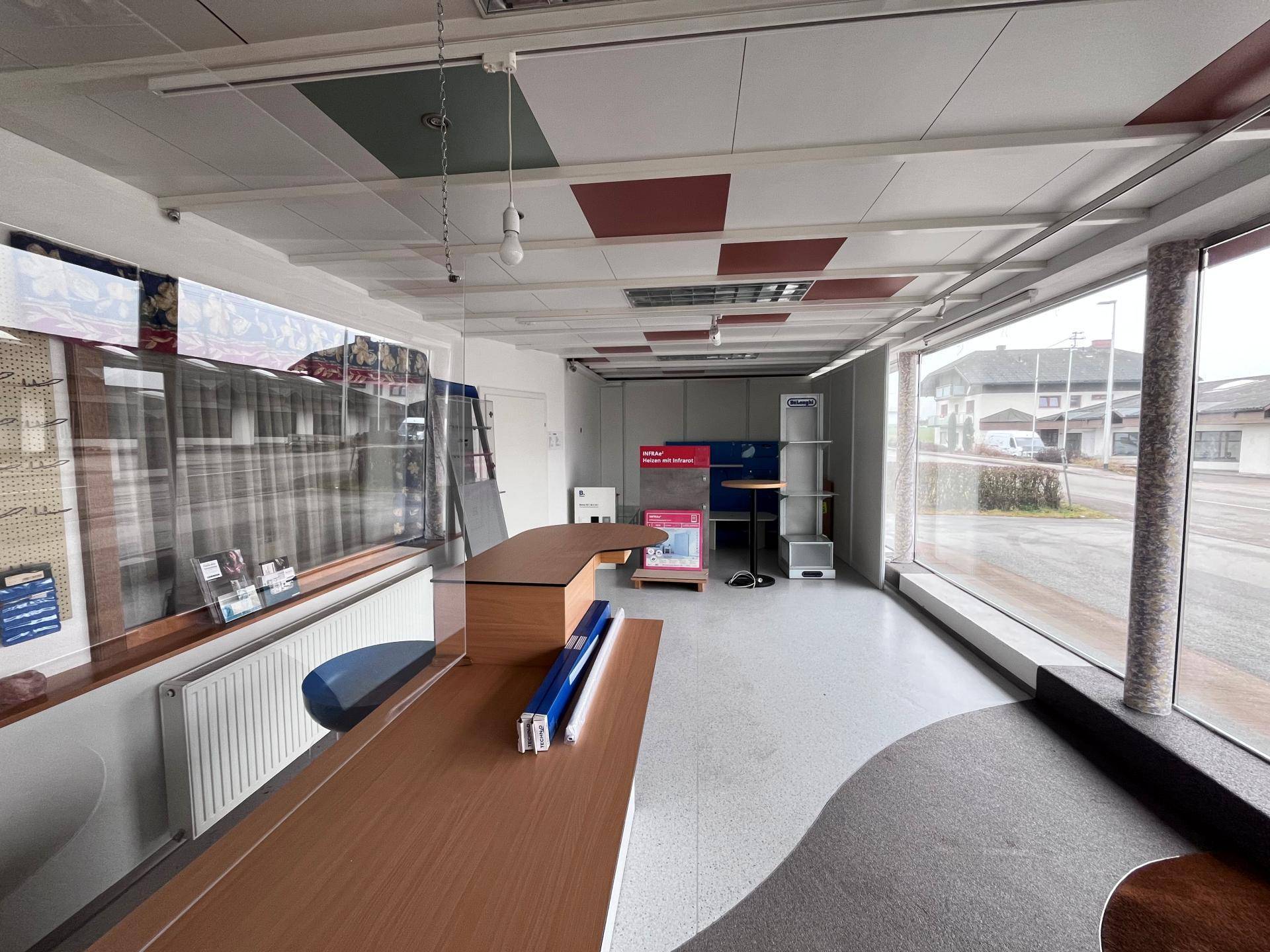 Leerer Ladenraum mit großen Schaufenstern, Teppichboden und einer Theke.