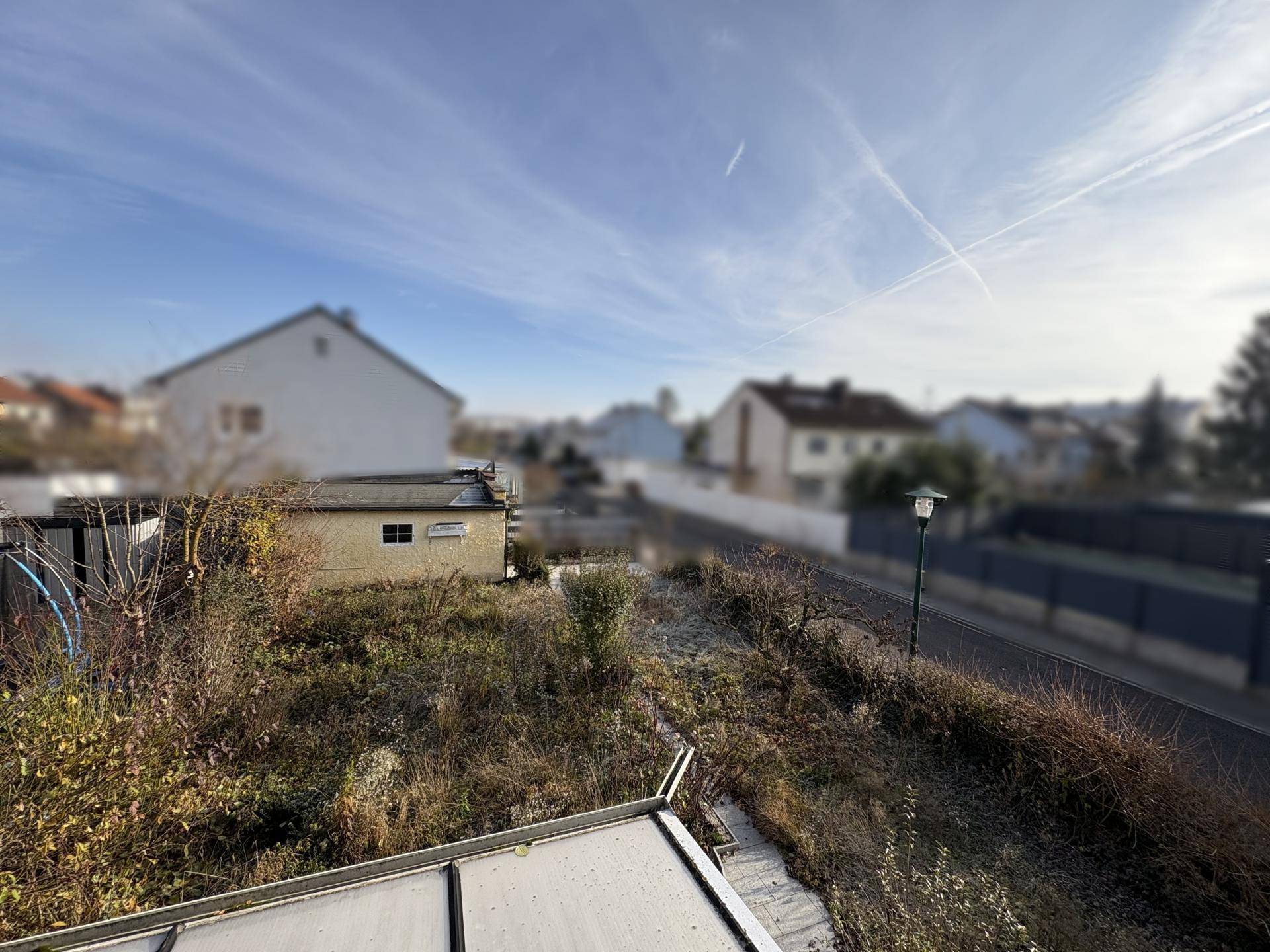 Blick über den verwilderten Garten mit einem kleinen Schuppen und der umliegenden Nachbarschaft.