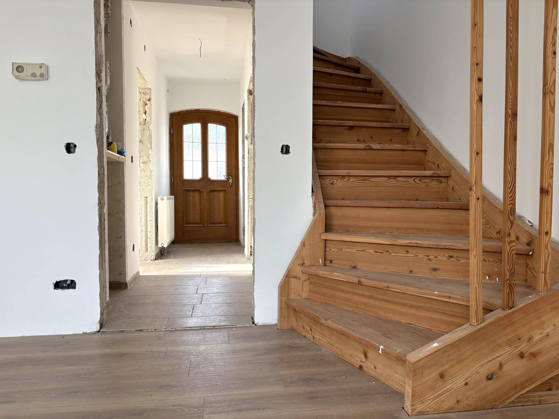 Holztreppe und Flur mit Fliesenboden, der zum Eingangsbereich des Hauses führt.