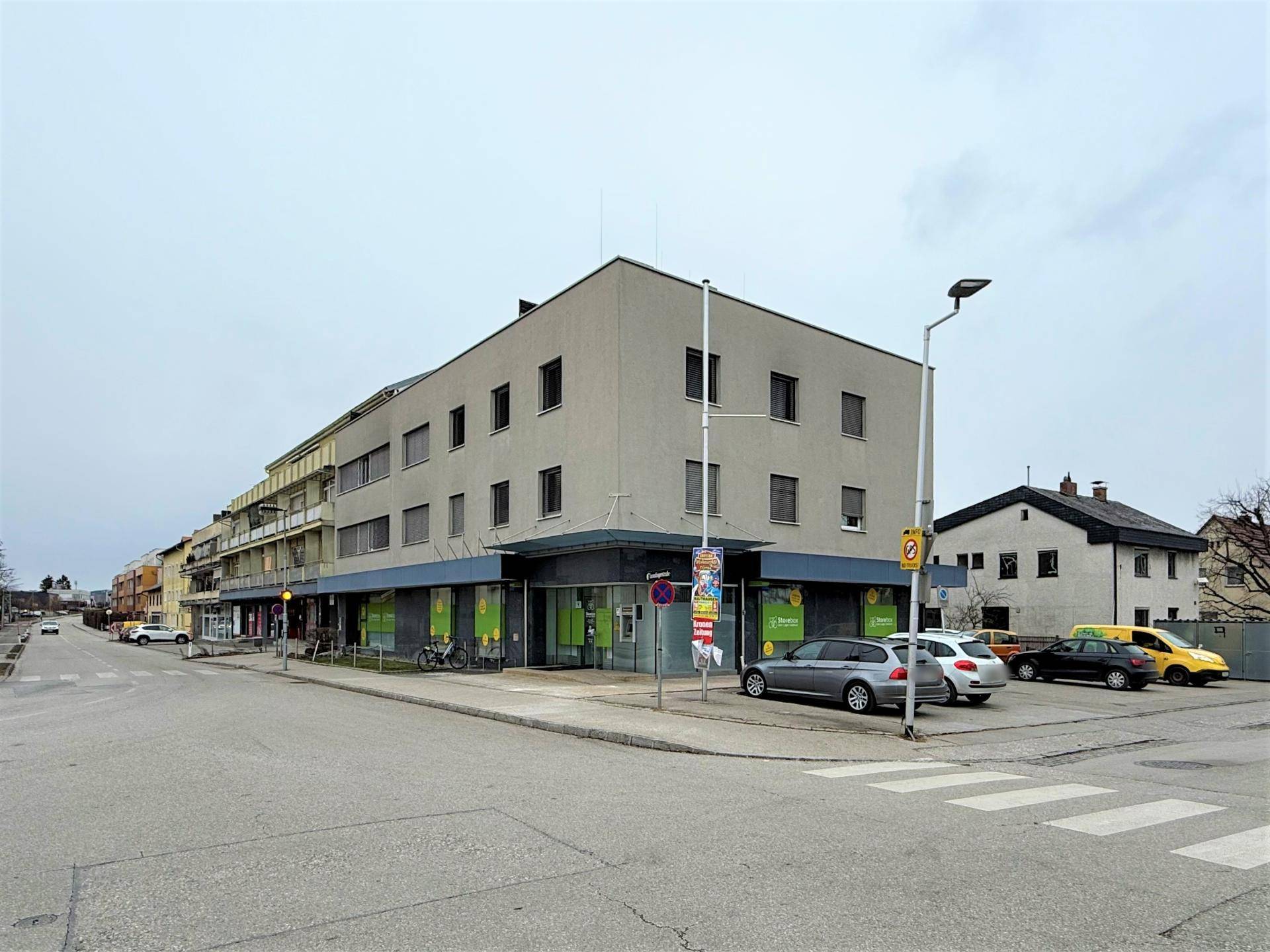 Mehrstöckiges Gebäude an einer Straßenecke mit Geschäften im Erdgeschoss, Teil einer städtischen Umgebung.