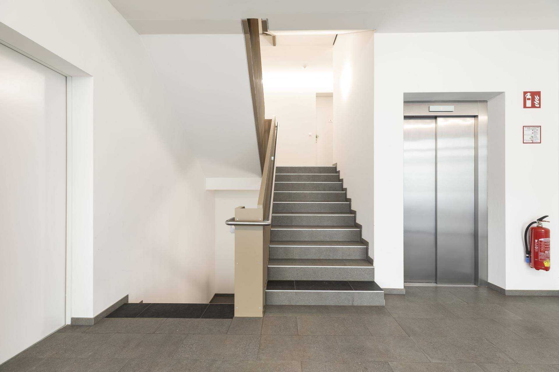 Eingangsbereich mit Treppe und modernem Aufzug, der Zugang zu den oberen Etagen bietet.