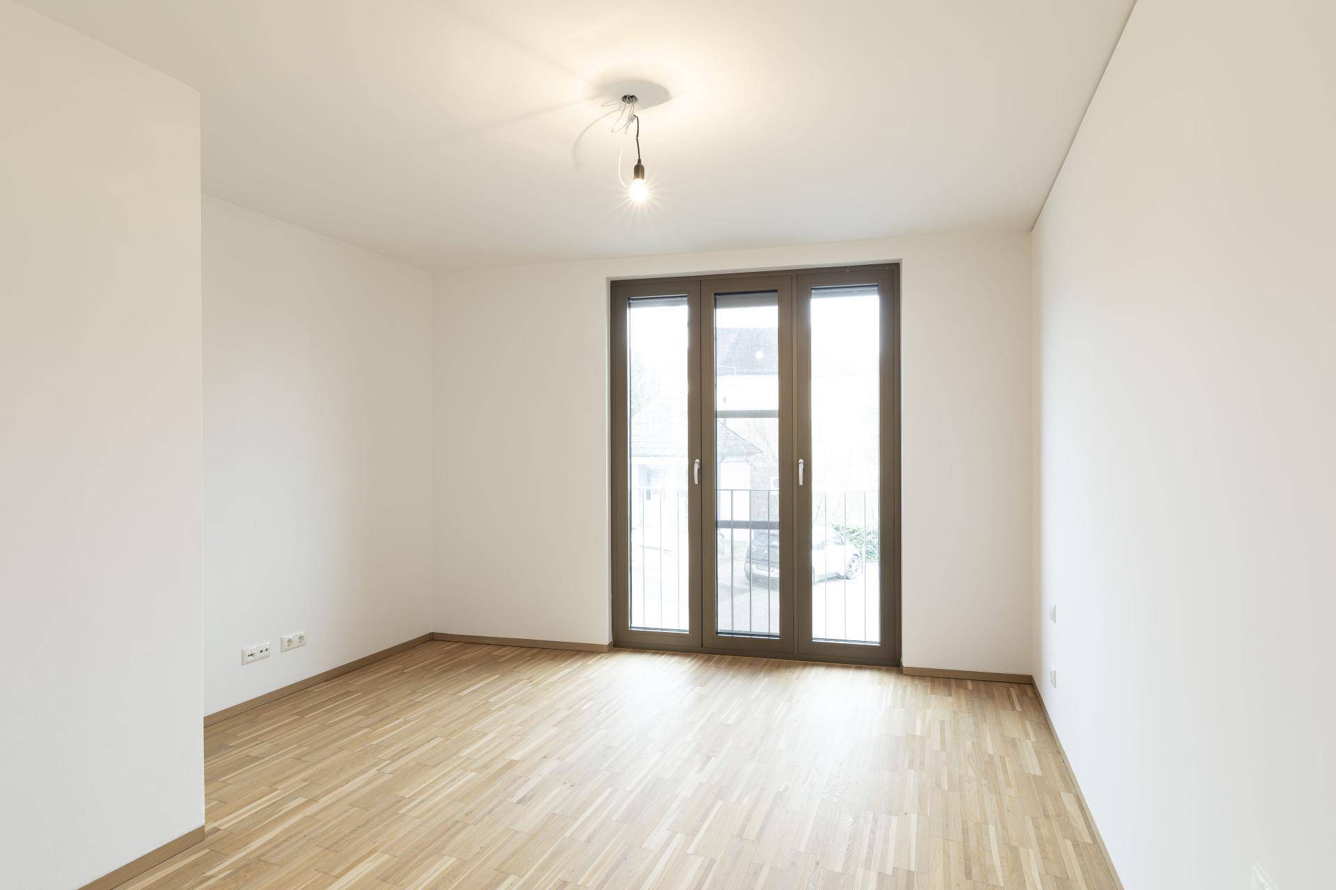 Leeres Schlafzimmer mit hellem Parkettboden und einer französischen Balkontür.