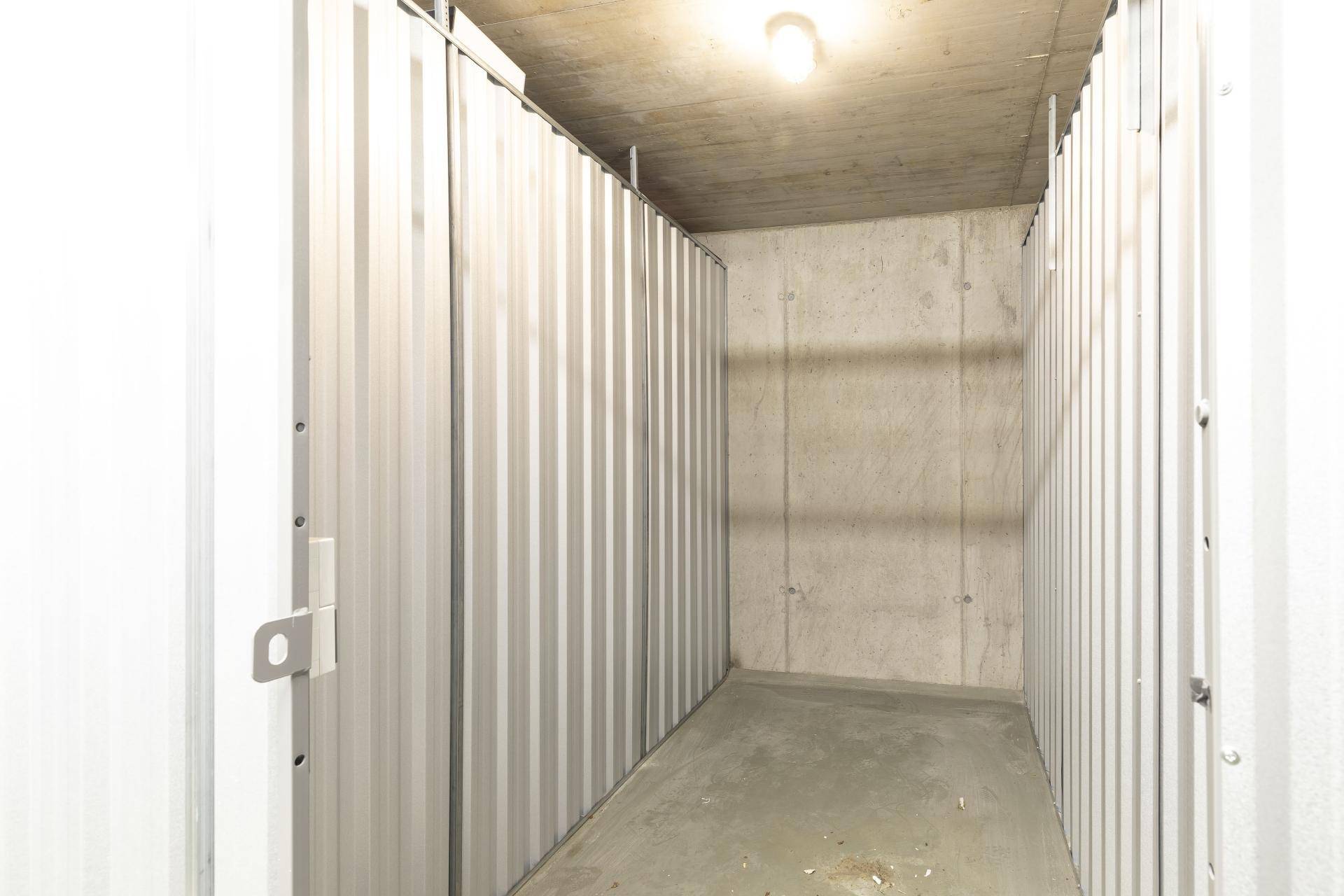 Funktionaler Abstellraum im Keller mit Betonboden und Metalltrennwand für zusätzlichen Stauraum.