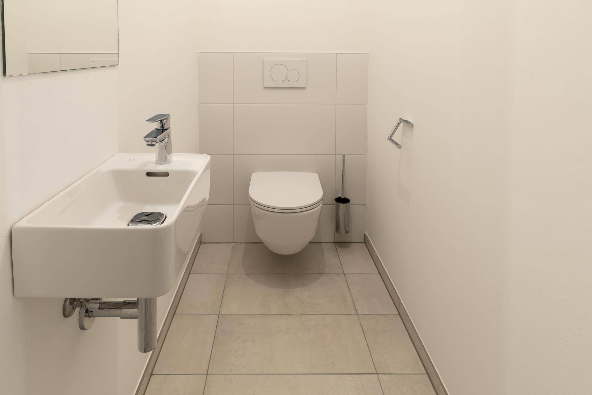 Helles Gäste-WC mit modernen Fliesen, wandhängendem WC und kleinem Waschbecken.