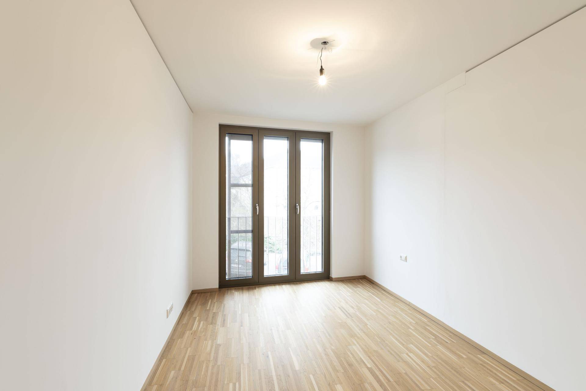 Leeres Zimmer mit hellem Parkettboden und einer französischen Balkontür, ideal als Schlafzimmer.