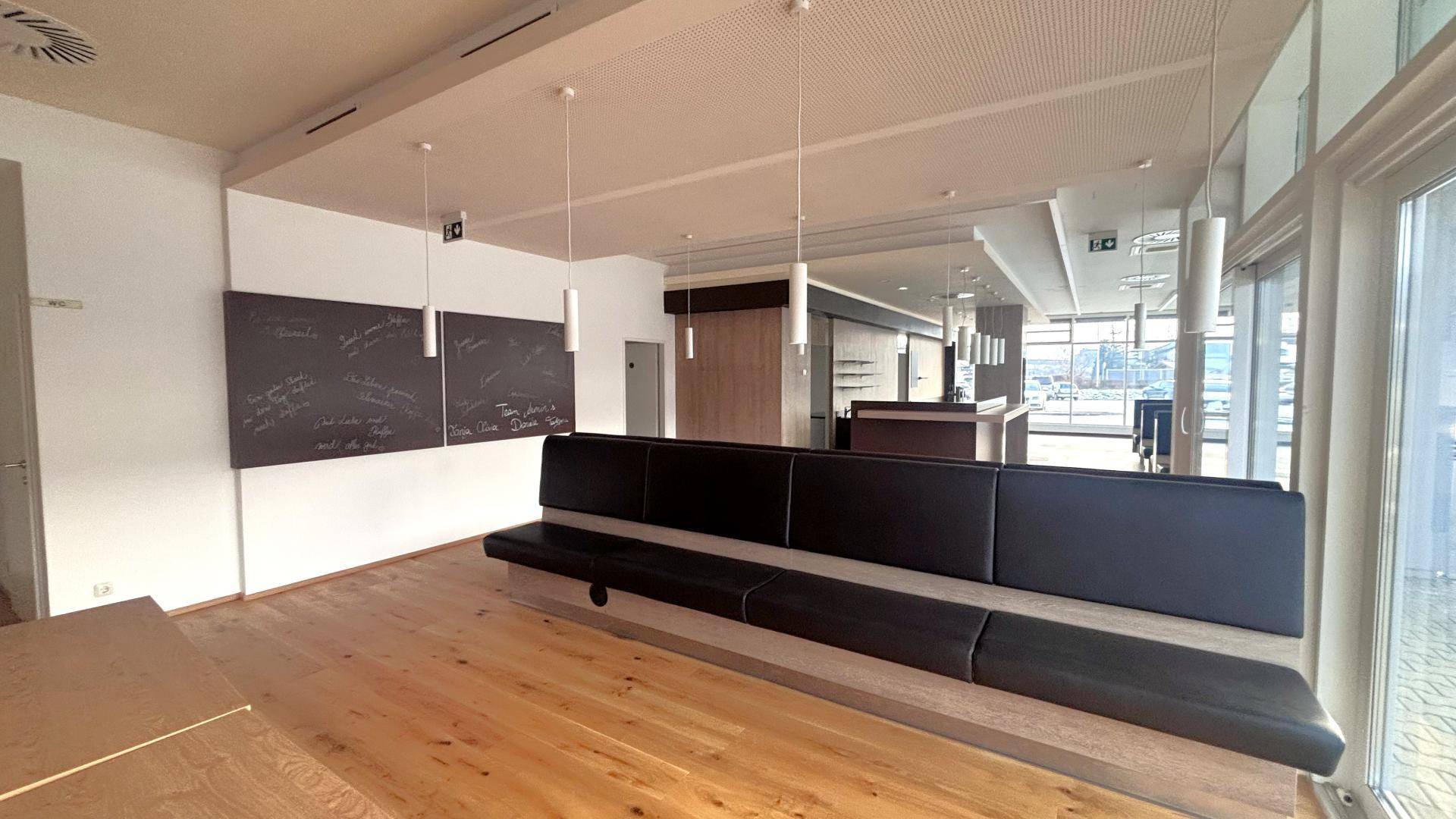 Offener Gewerbebereich mit Holzboden, langer Sitzbank und großen Fenstern, die viel Tageslicht hereinlassen.