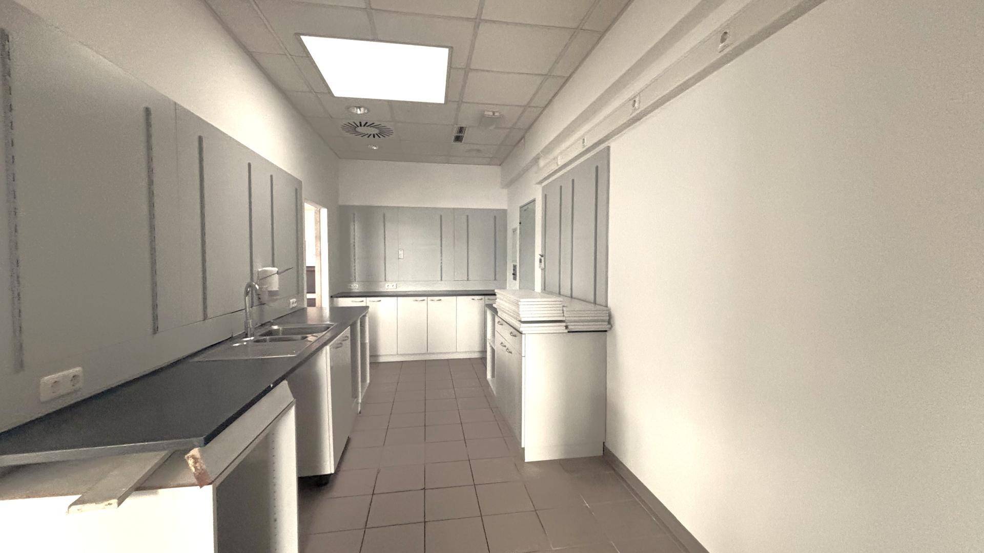 Funktionale Gewerbeküche mit Edelstahlspülen, weißen Unterschränken und Fliesenboden für den Betrieb.