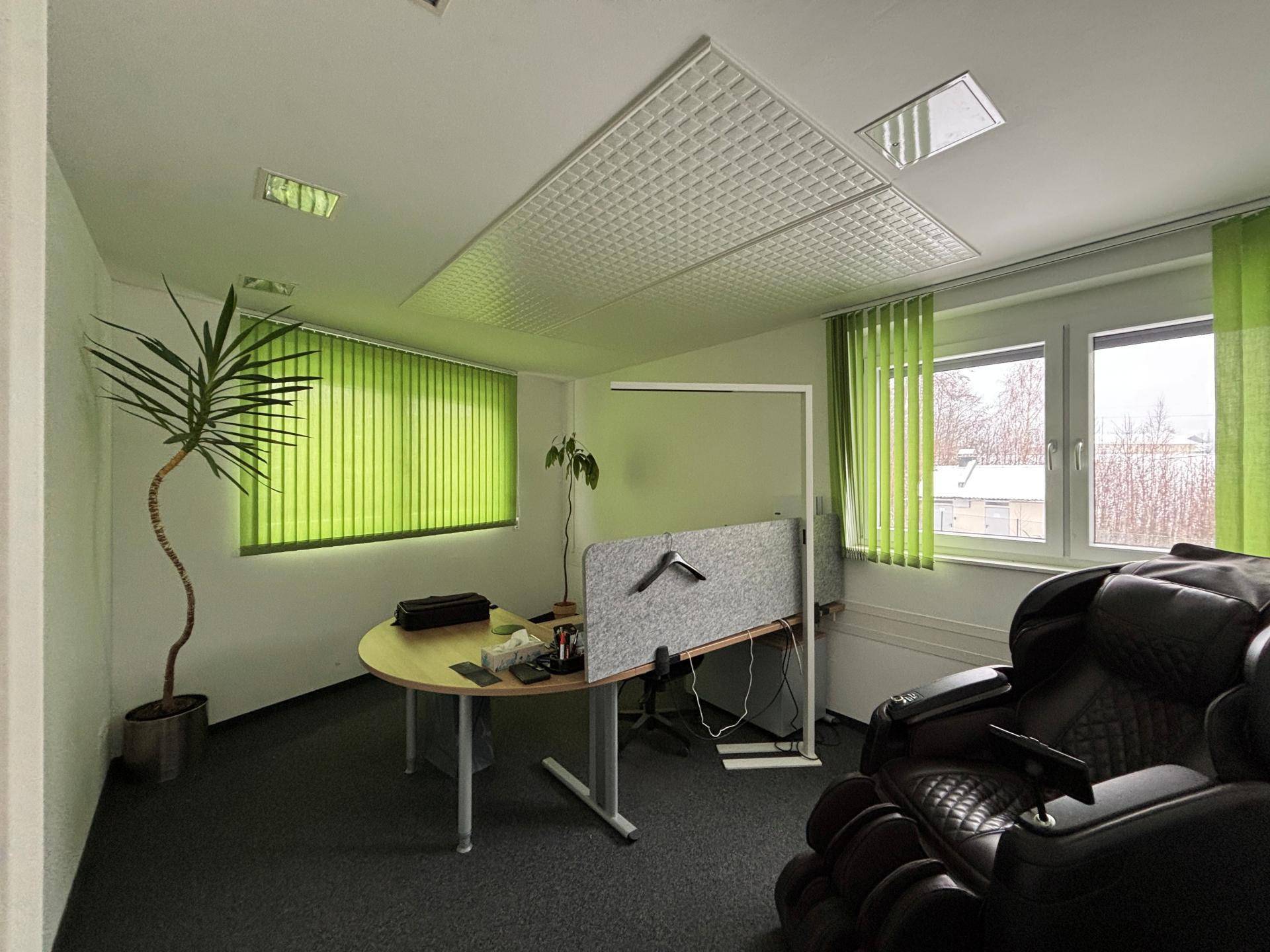 Geräumiges Büro mit Schreibtisch, Massagesessel und hellgrünen Jalousien an den Fenstern.