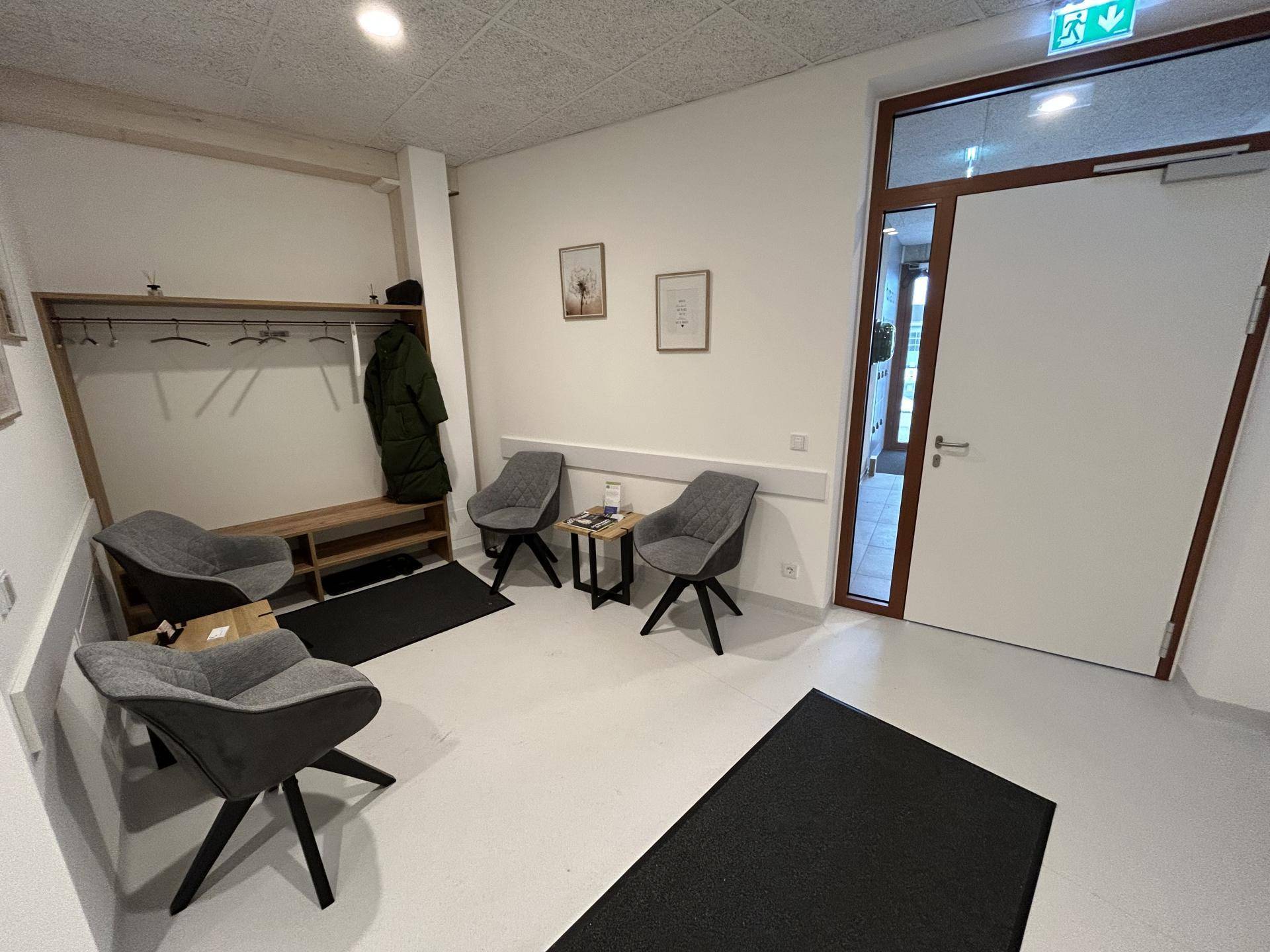 Einladender Wartebereich mit bequemen Stühlen, Garderobe und Zugang zu weiteren Räumen.