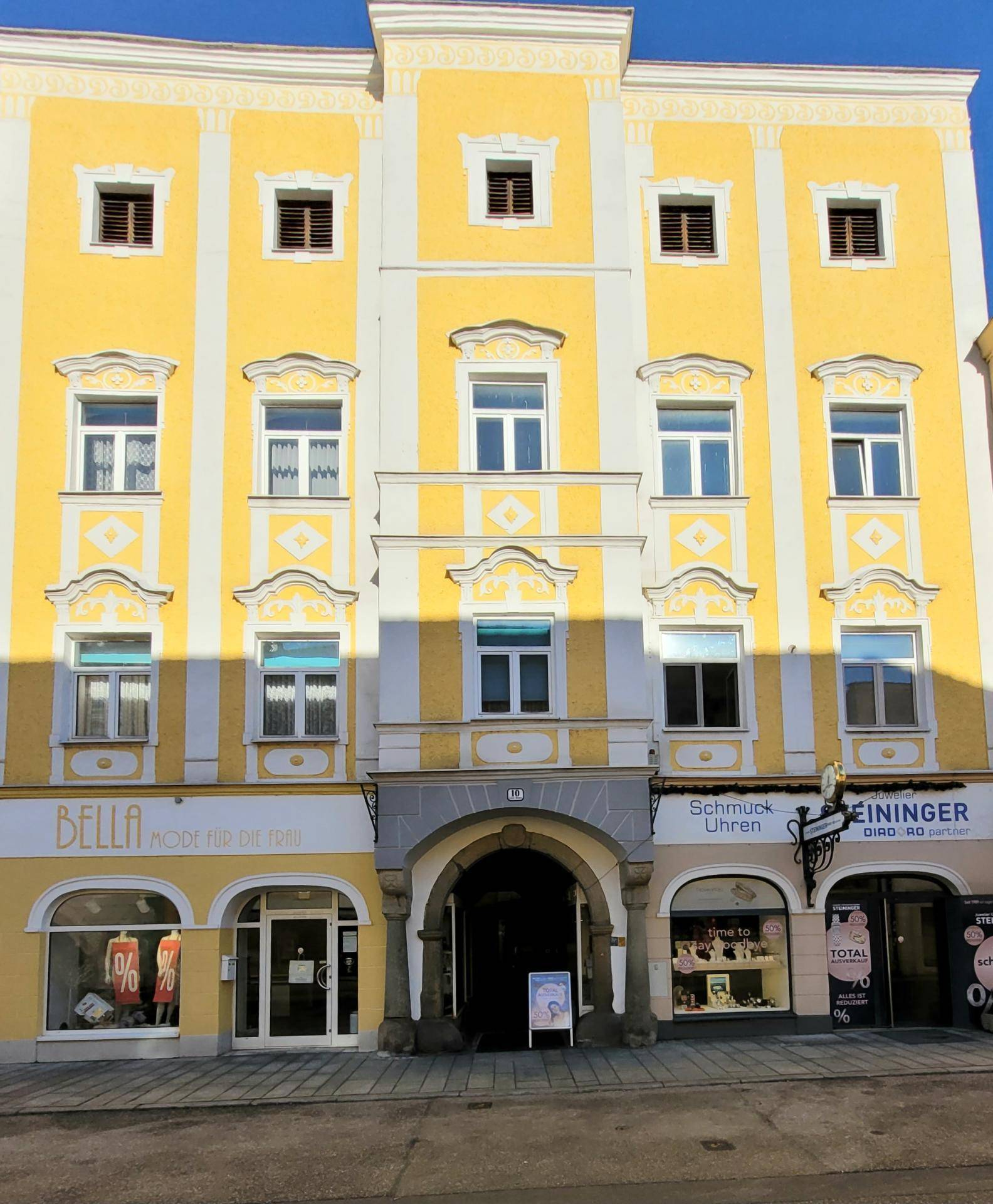 Historische Fassade eines Gebäudes mit gelben und weißen Elementen sowie Geschäften im Erdgeschoss.