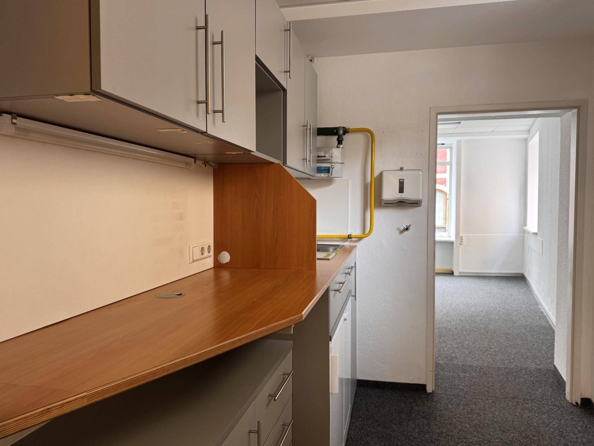 Praktische Küchenzeile mit Holz-Arbeitsplatte und grauen Unterschränken, die in einen weiteren Raum führt.