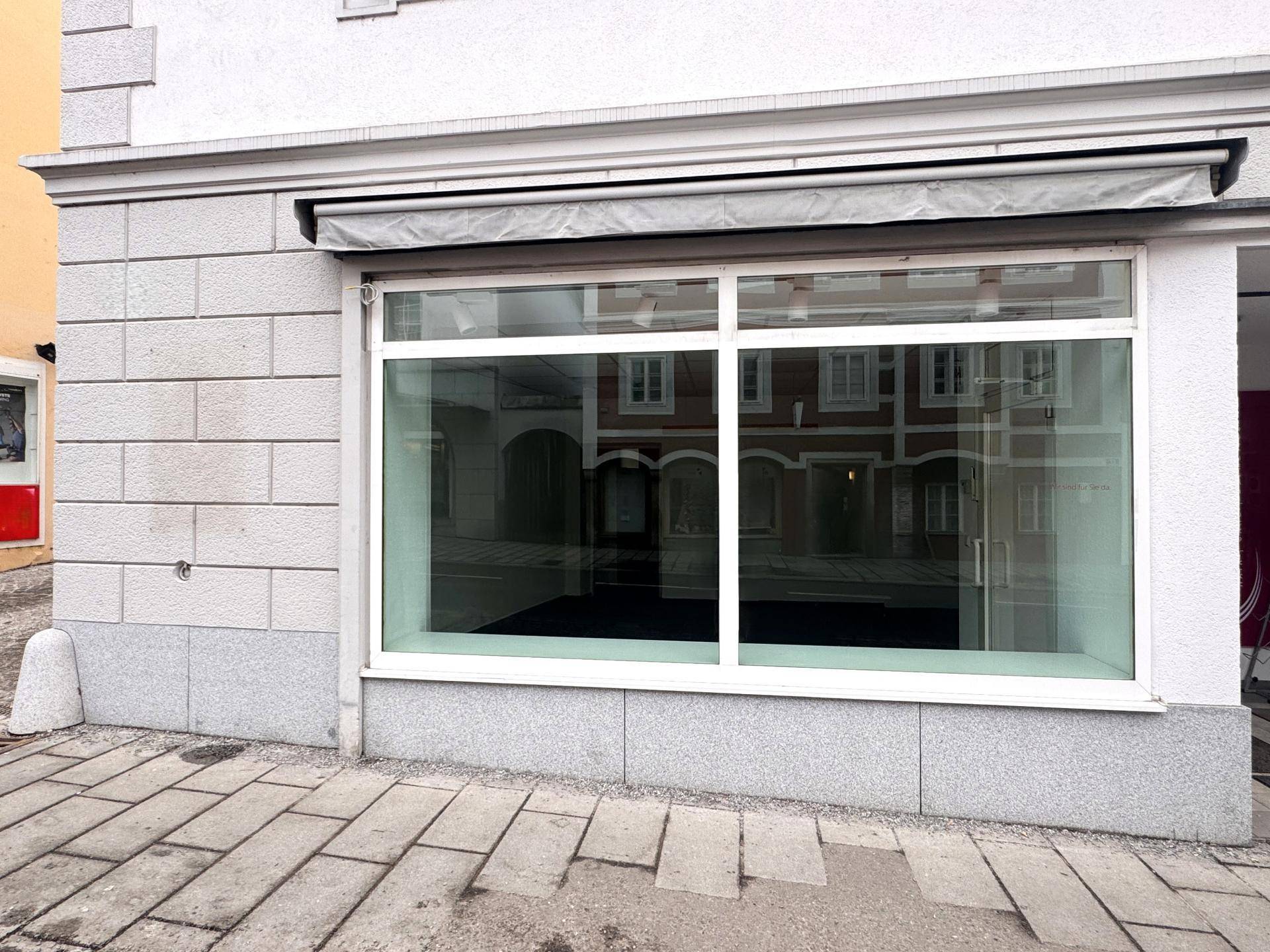 Nahaufnahme der Geschäftsfassade mit großen, sauberen Schaufenstern und einem grauen Sonnenschutz über dem Eingang.