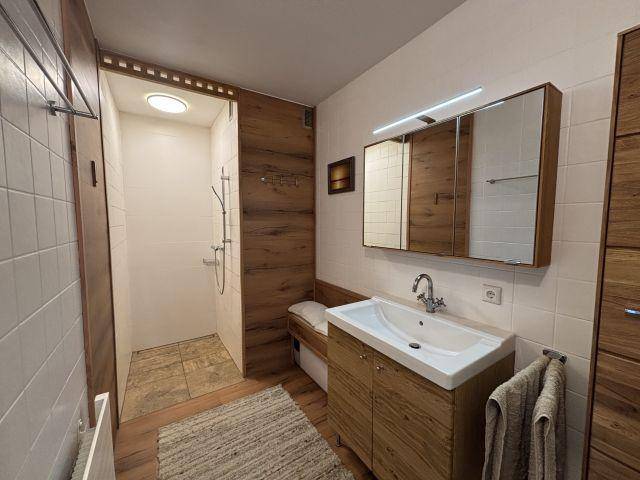 Modernes Badezimmer mit begehbarer Dusche, Holzoptik-Möbeln und weiß gefliesten Wänden.