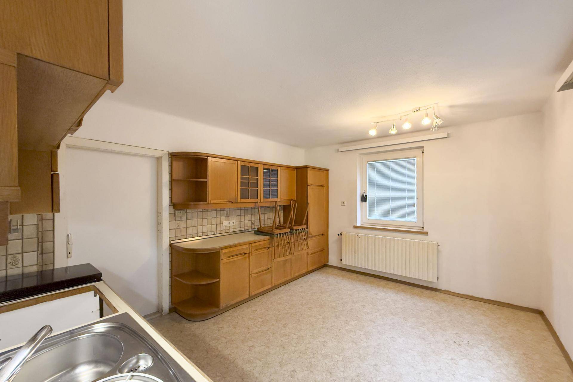 Küche mit älteren Holzschränken, Fliesenrückwand und Platz für einen Essbereich.