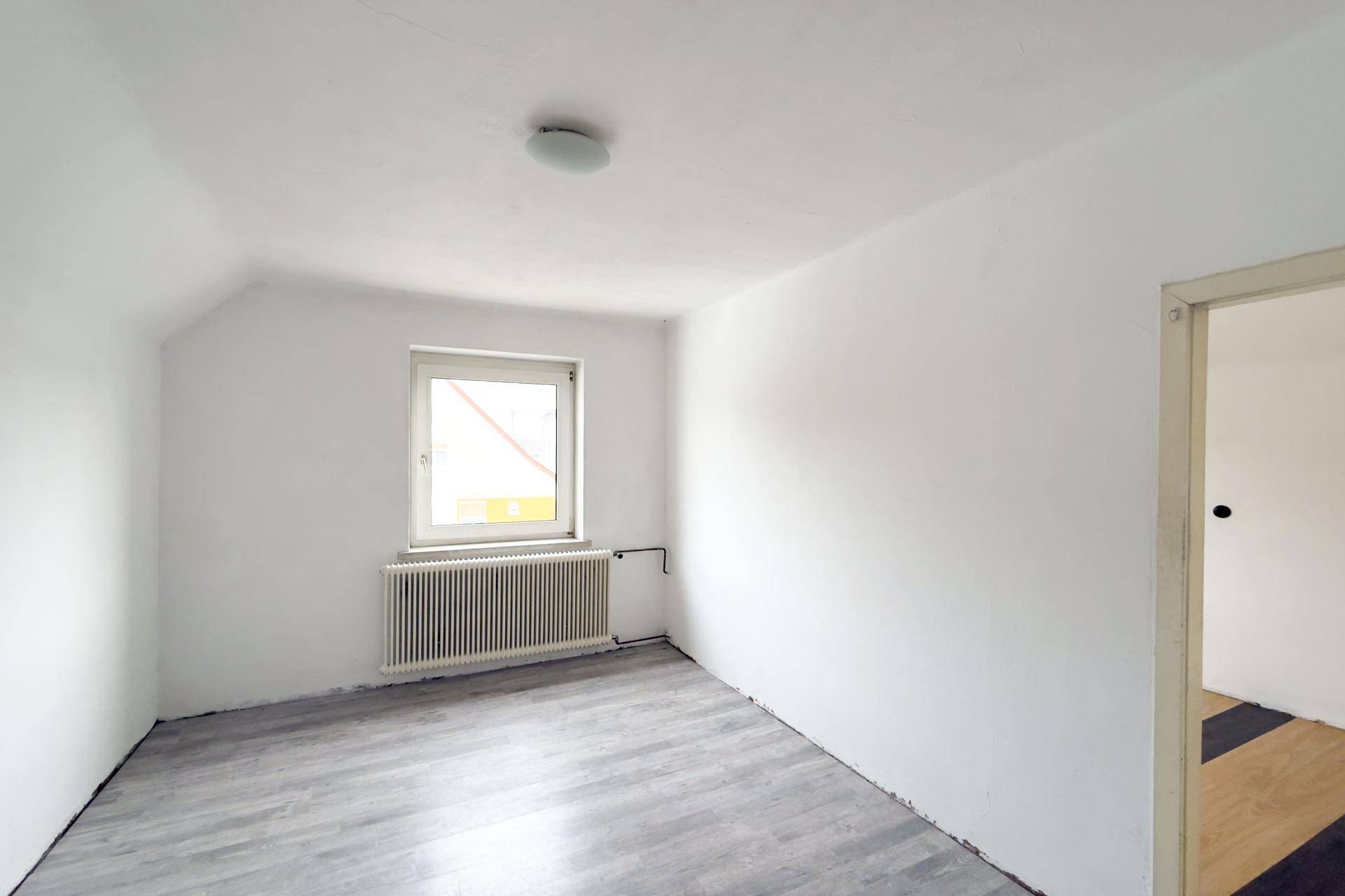 Helles Schlafzimmer mit weiß gestrichenen Wänden, Dachschräge und Laminatboden.