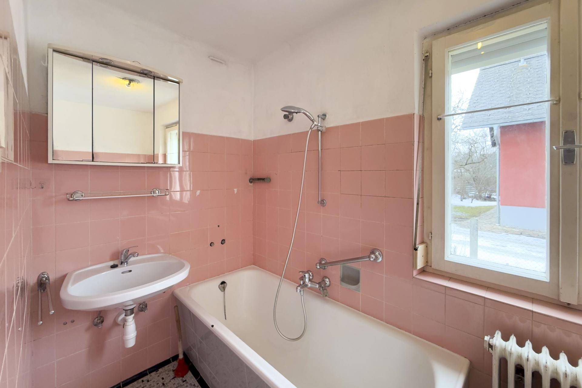 Badezimmer im 80er-Jahre-Stil mit rosa Fliesen, Badewanne, Waschbecken und Fenster.