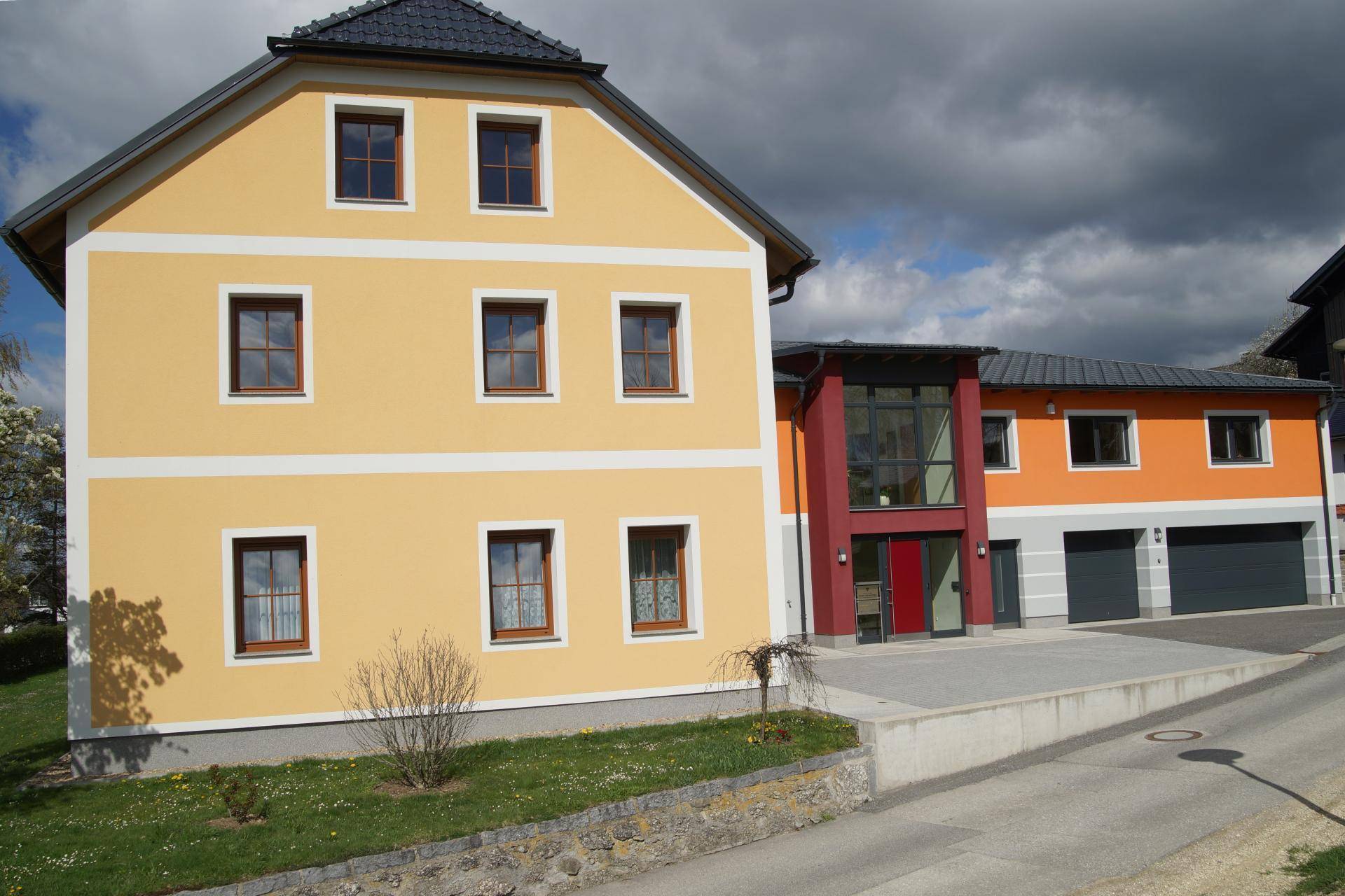 Ansicht des modernen Gebäudes mit gelbem Nachbarhaus und gepflegter Grünfläche.