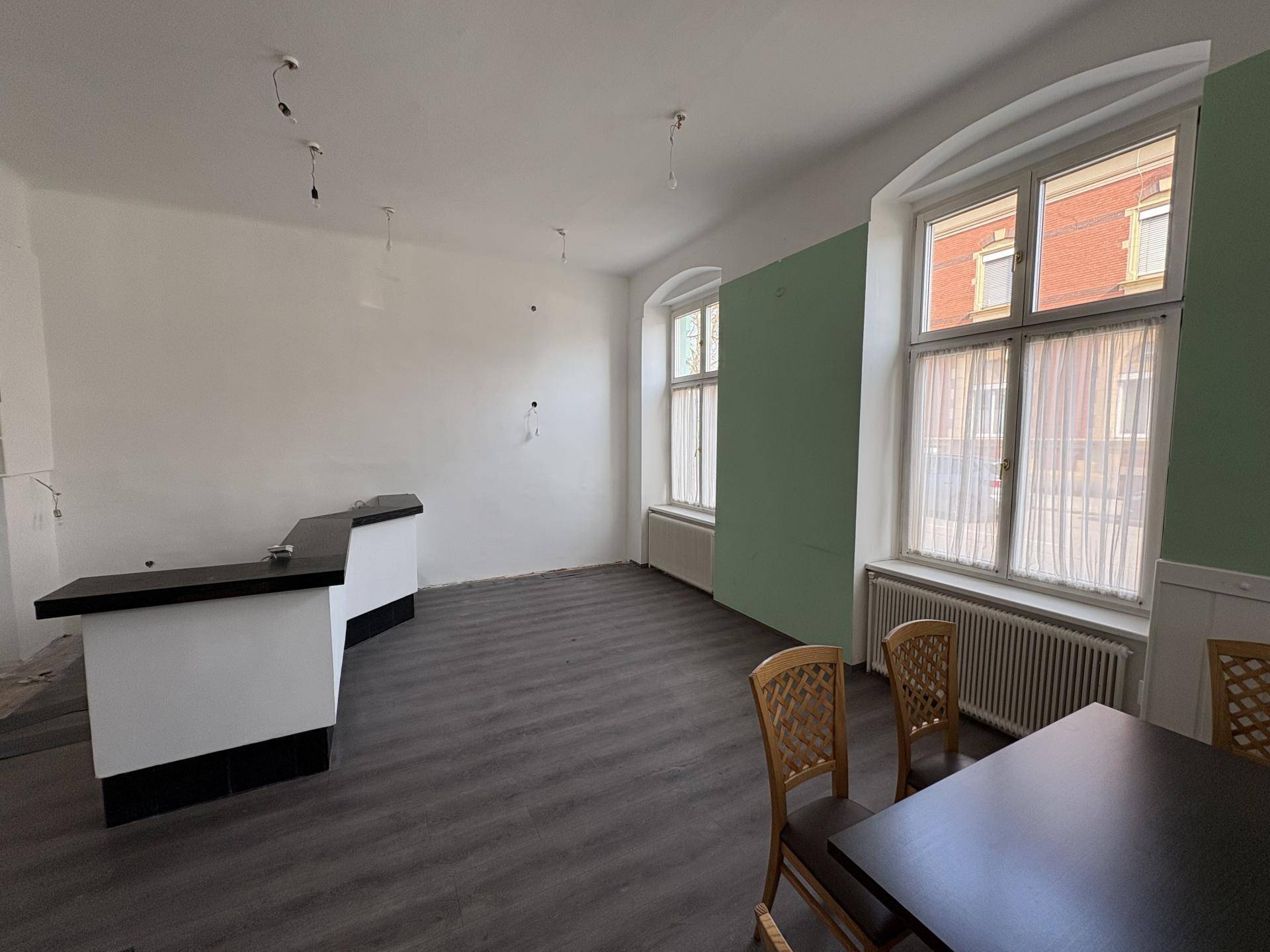 Raum mit Bar, dunklem Boden und großen Fenstern mit Heizkörpern darunter, teilweise hellgrüne Wand.