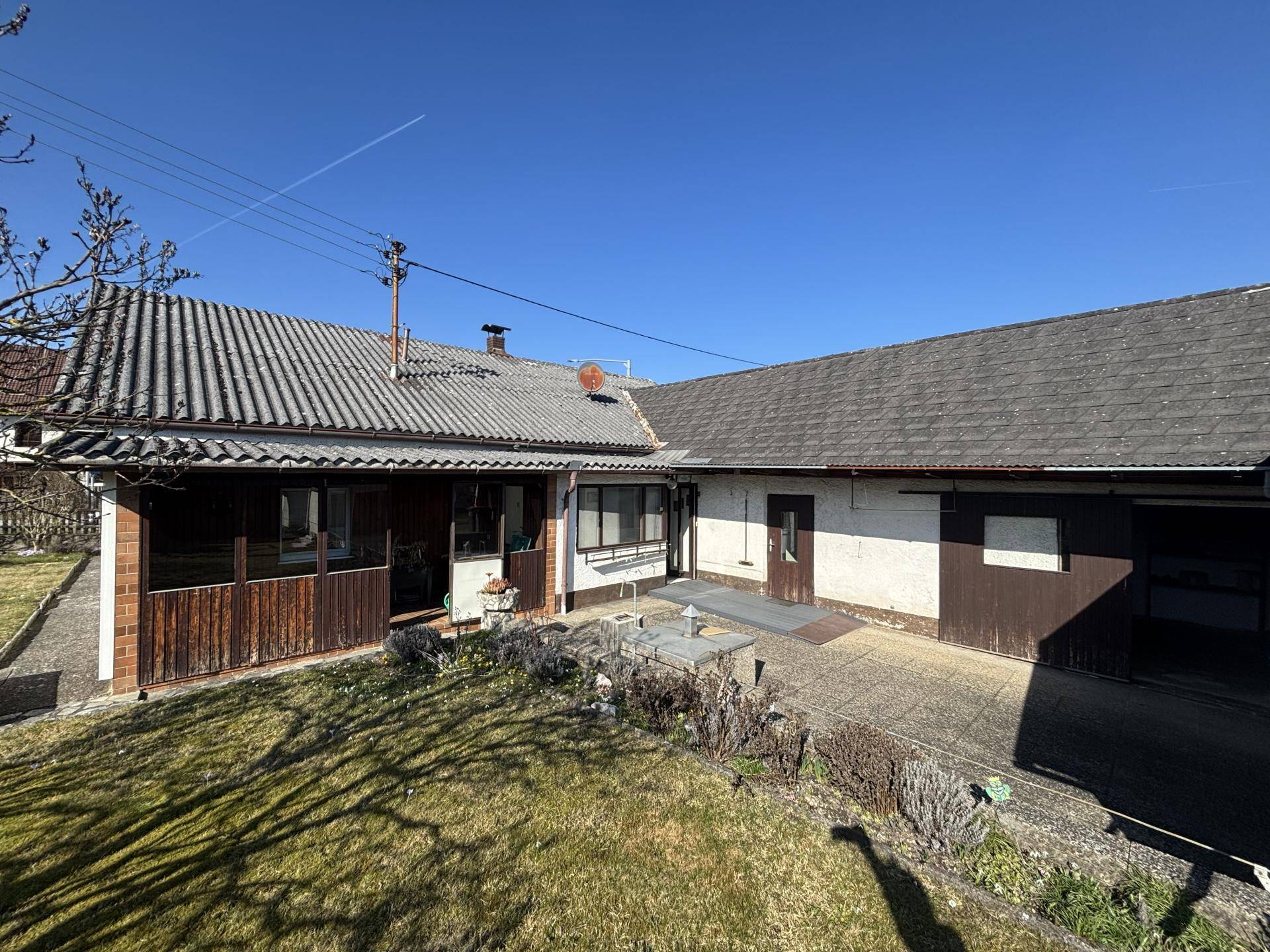 Rückansicht des Hauses mit überdachtem Bereich, Garten und Satteldach unter klarem Himmel.