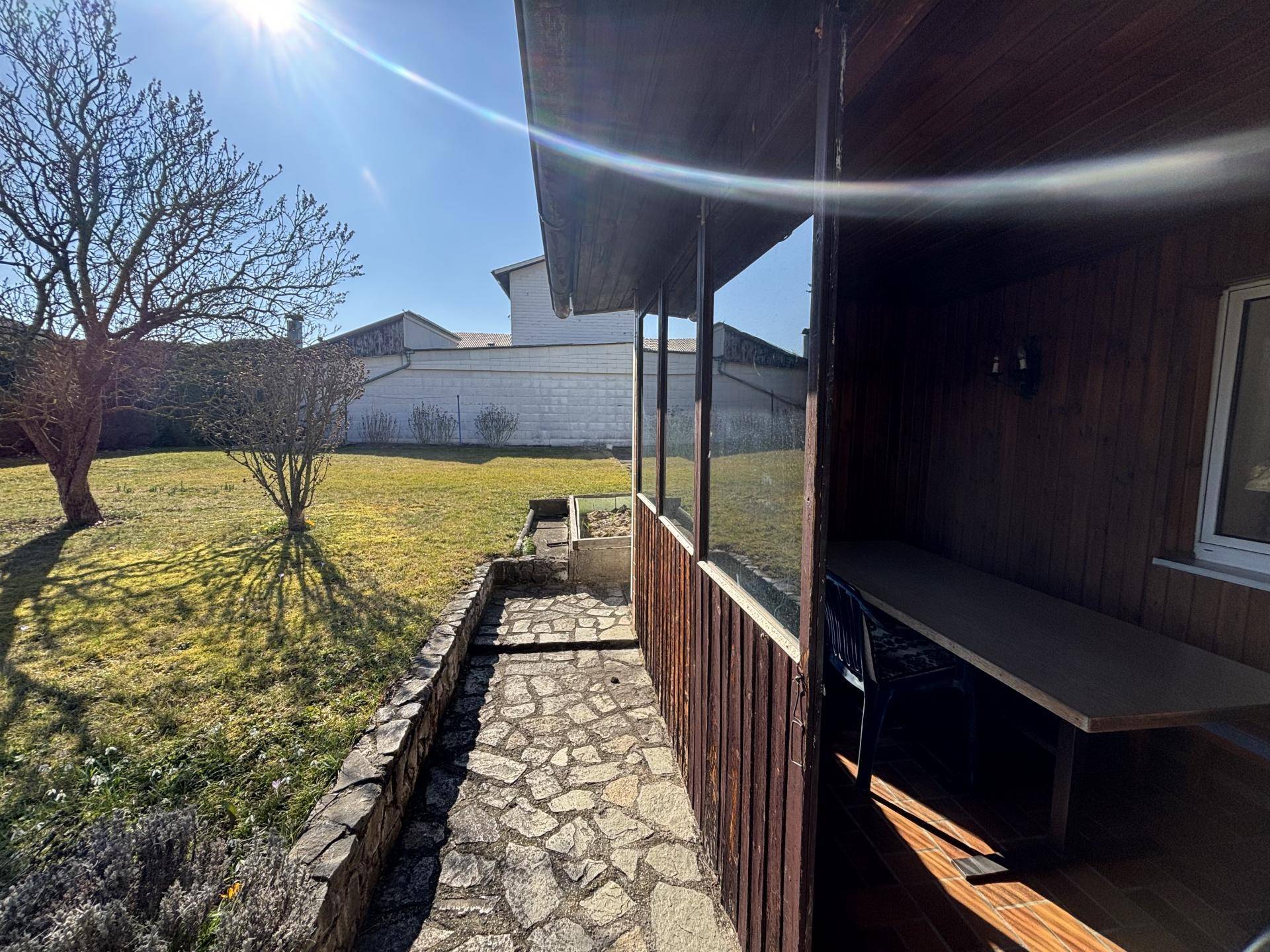 Überdachte Terrasse mit Holzwänden und Steinweg, angrenzend an einen sonnigen Garten.