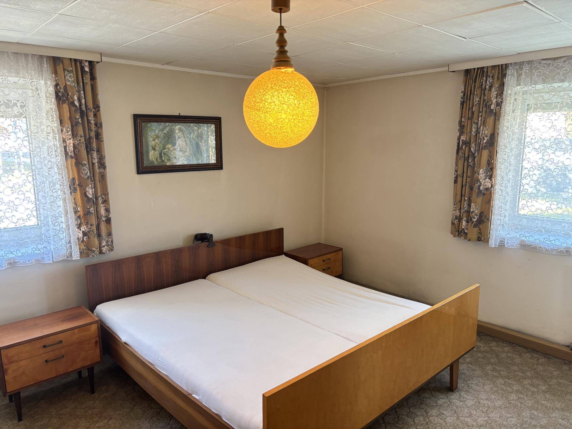 Schlafzimmer mit Doppelbett, Nachttischen und zwei Fenstern für natürliches Licht.