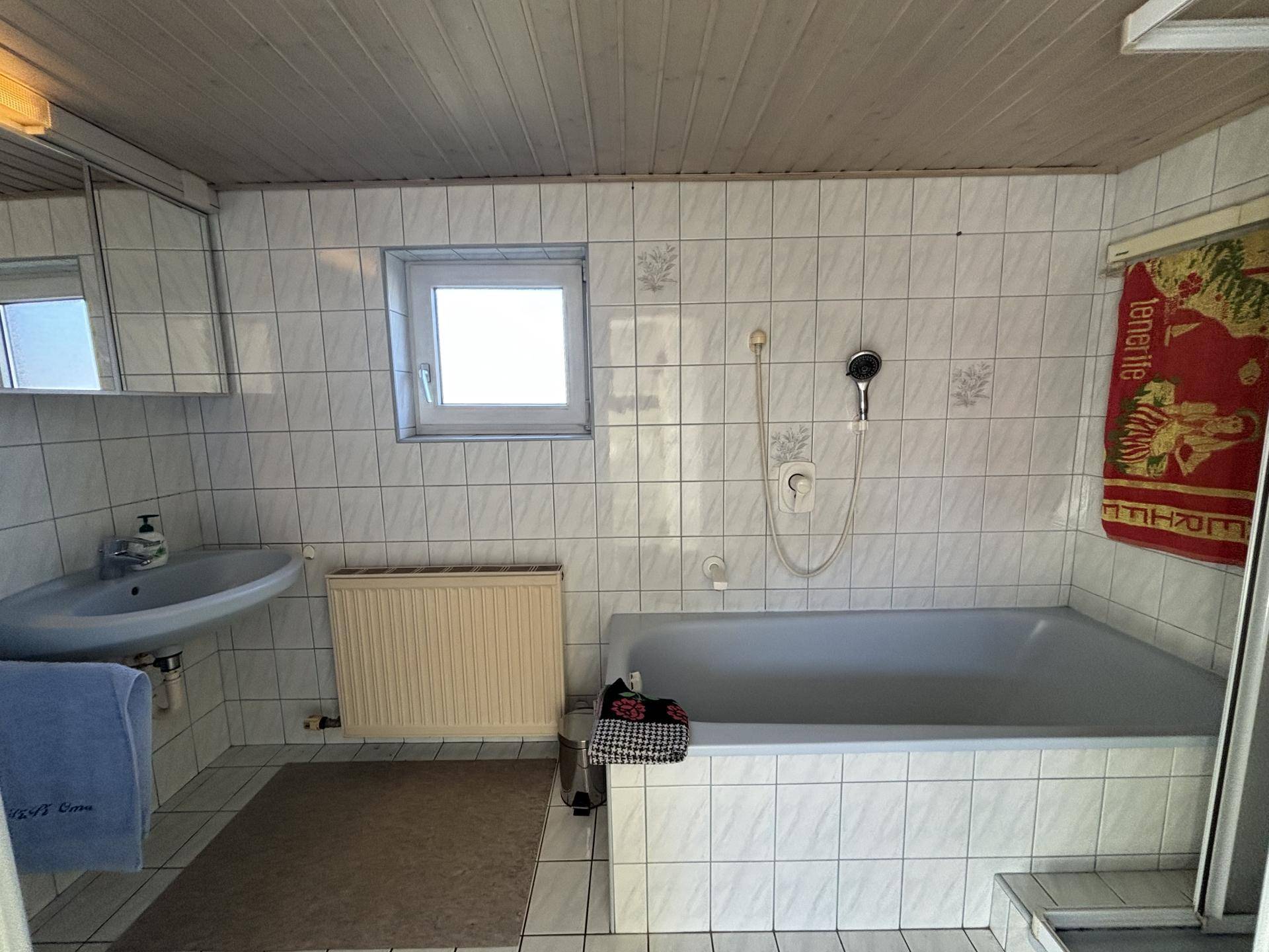 Gefliestes Badezimmer mit Badewanne, Waschbecken und Fenster für Belüftung.