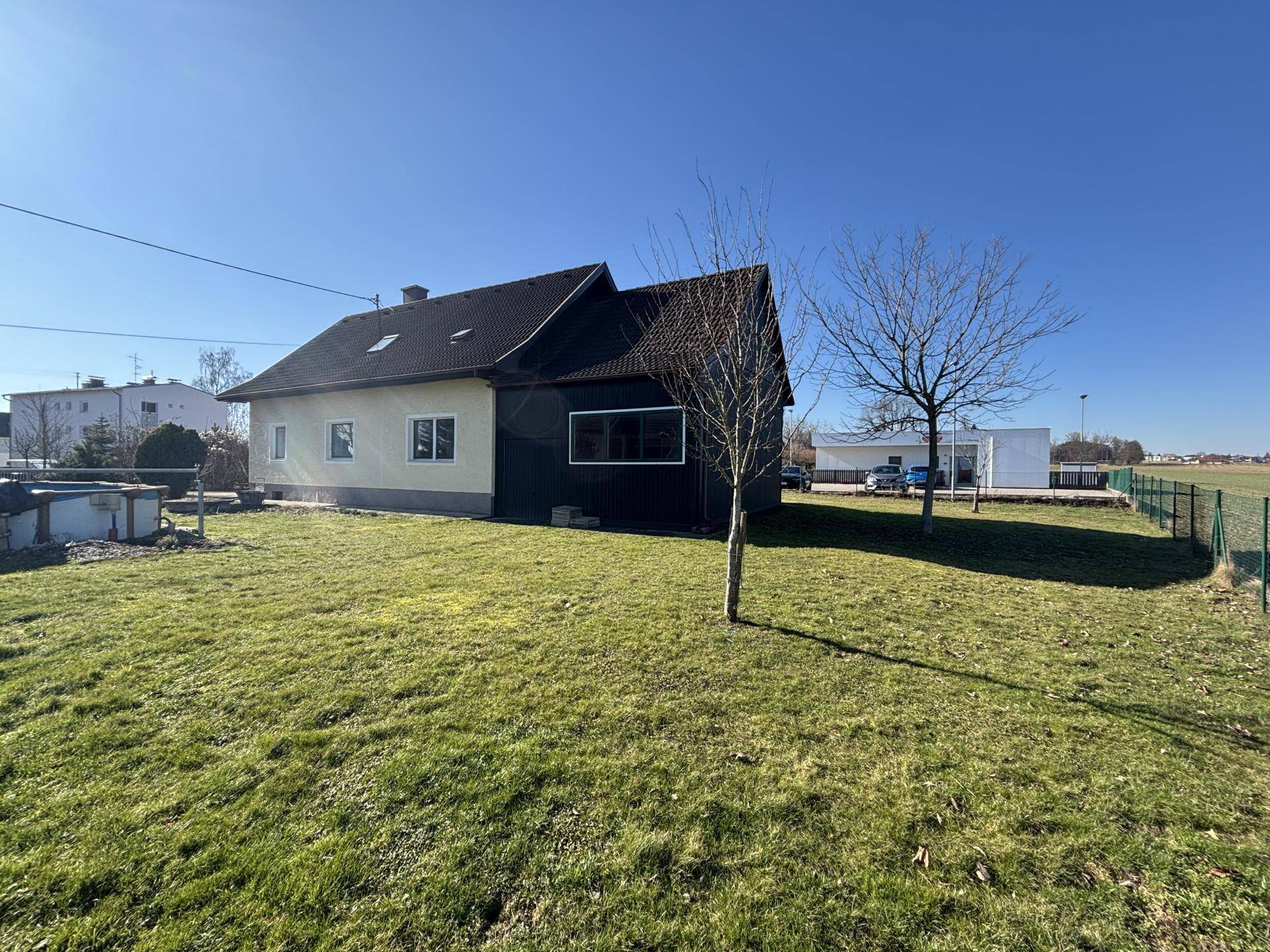 Rückansicht des Hauses mit großem Rasenbereich und angrenzendem Zaun unter blauem Himmel.