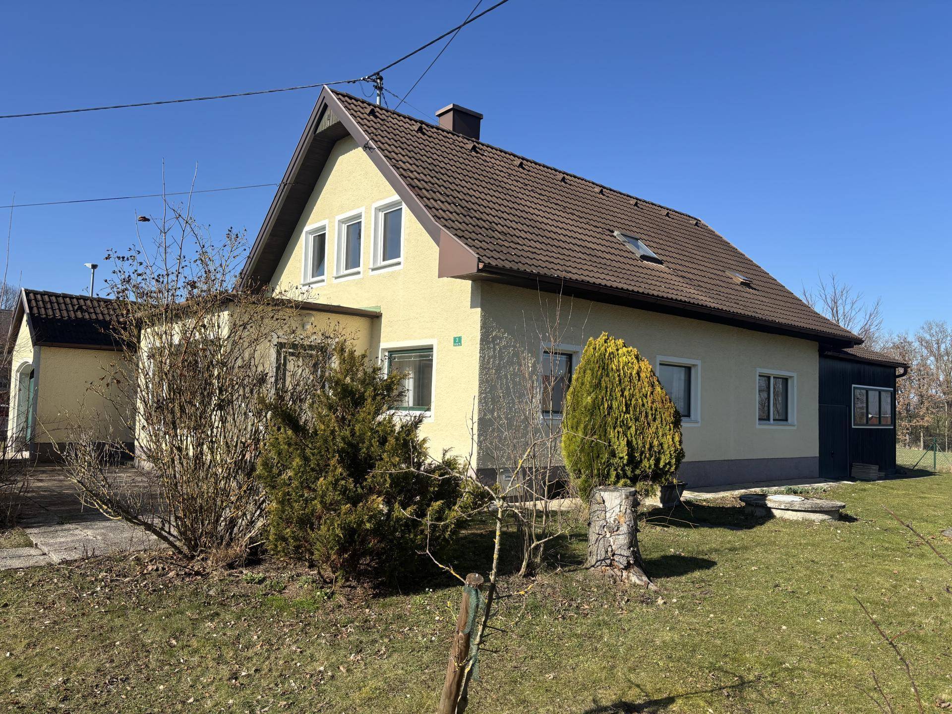Seitenansicht des gelben Hauses mit braunem Ziegeldach und gepflegtem Gartenbereich.
