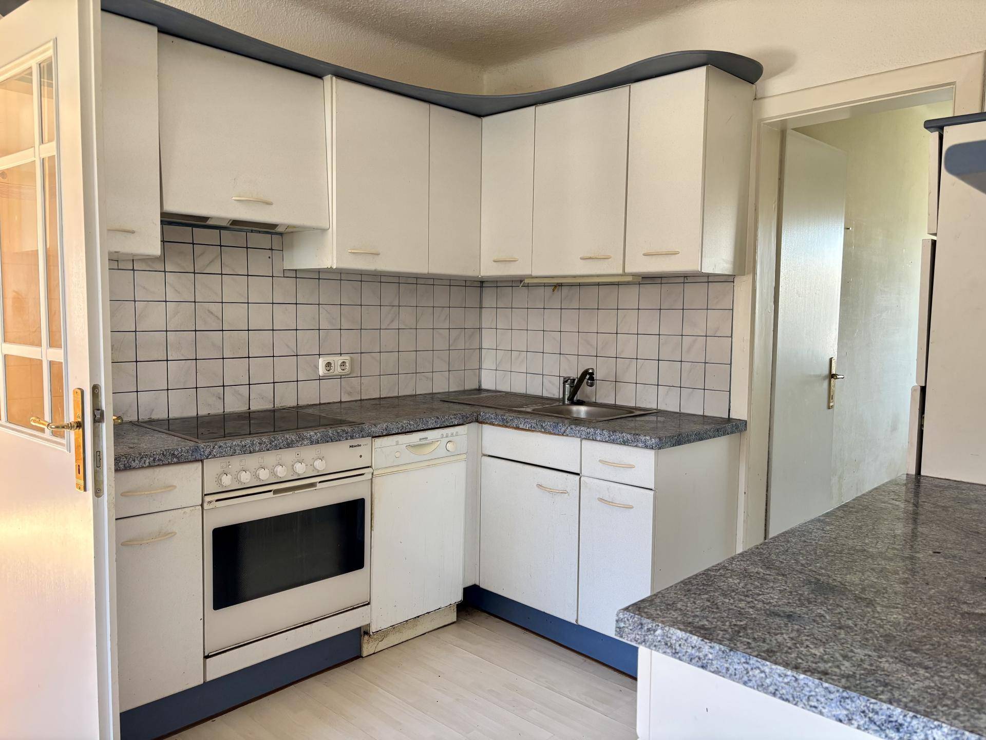 Funktionale Eckküche mit weißen Schränken, blauen Arbeitsplatten und Fliesenrückwand.