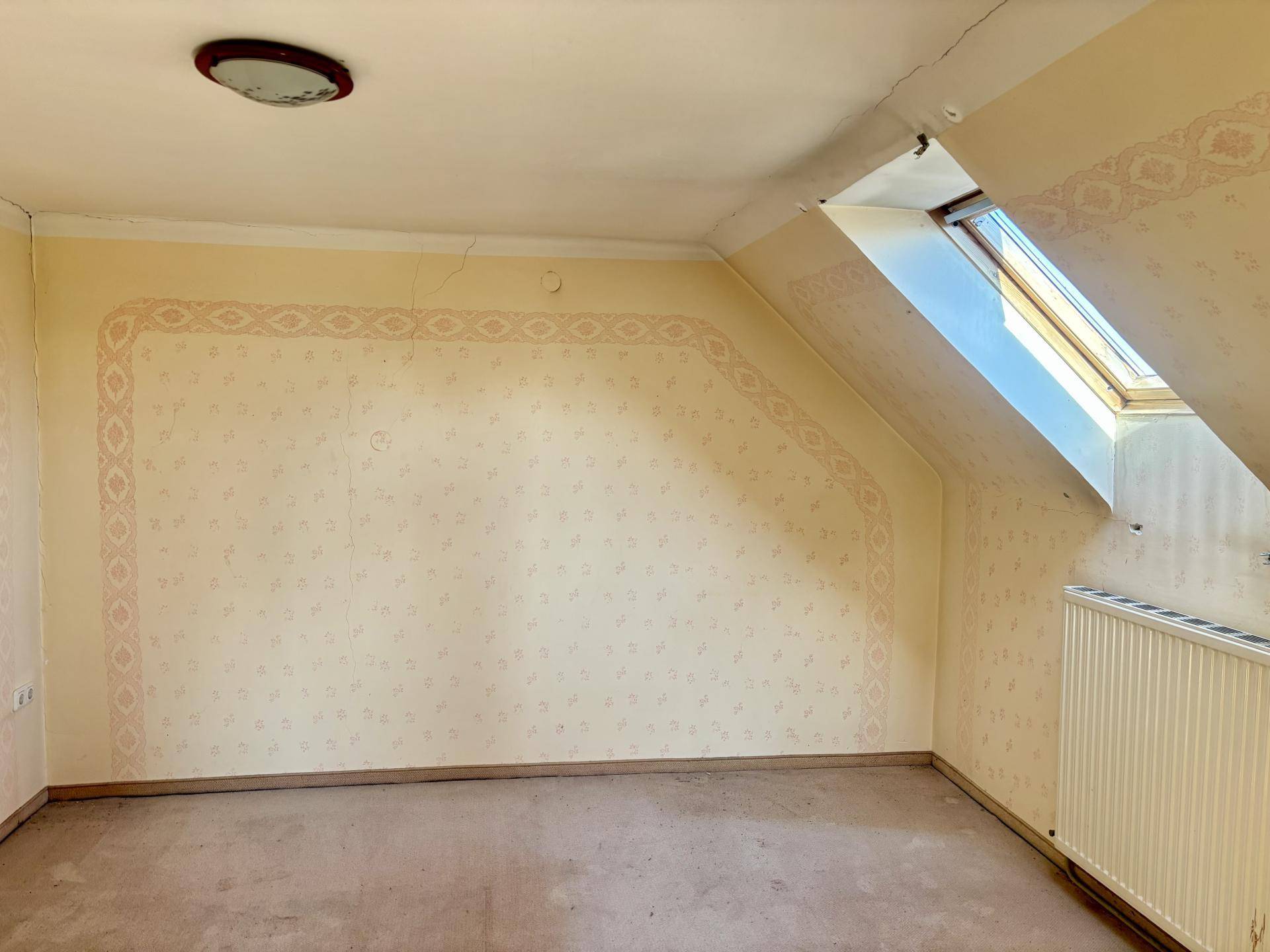 Dachzimmer mit schräger Decke, Dachfenster und gemusterter Tapete, bereit zur Gestaltung.