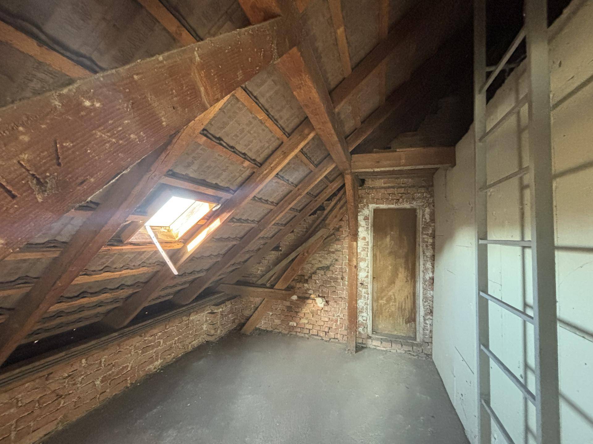 Unausgebauter Dachboden mit sichtbaren Holzbalken, Ziegelwänden und Dachfenster.