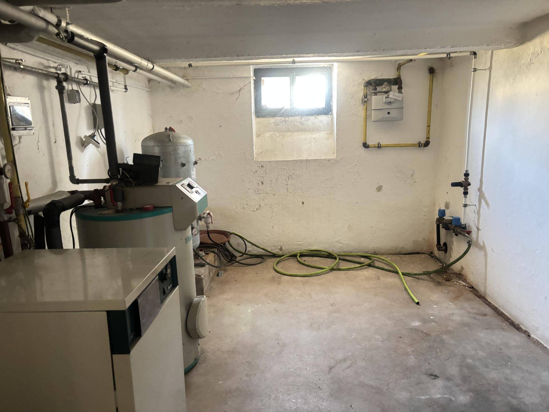 Kellerraum mit Heizungsanlage, Leitungen und kleinem Fenster, als Technikraum genutzt.