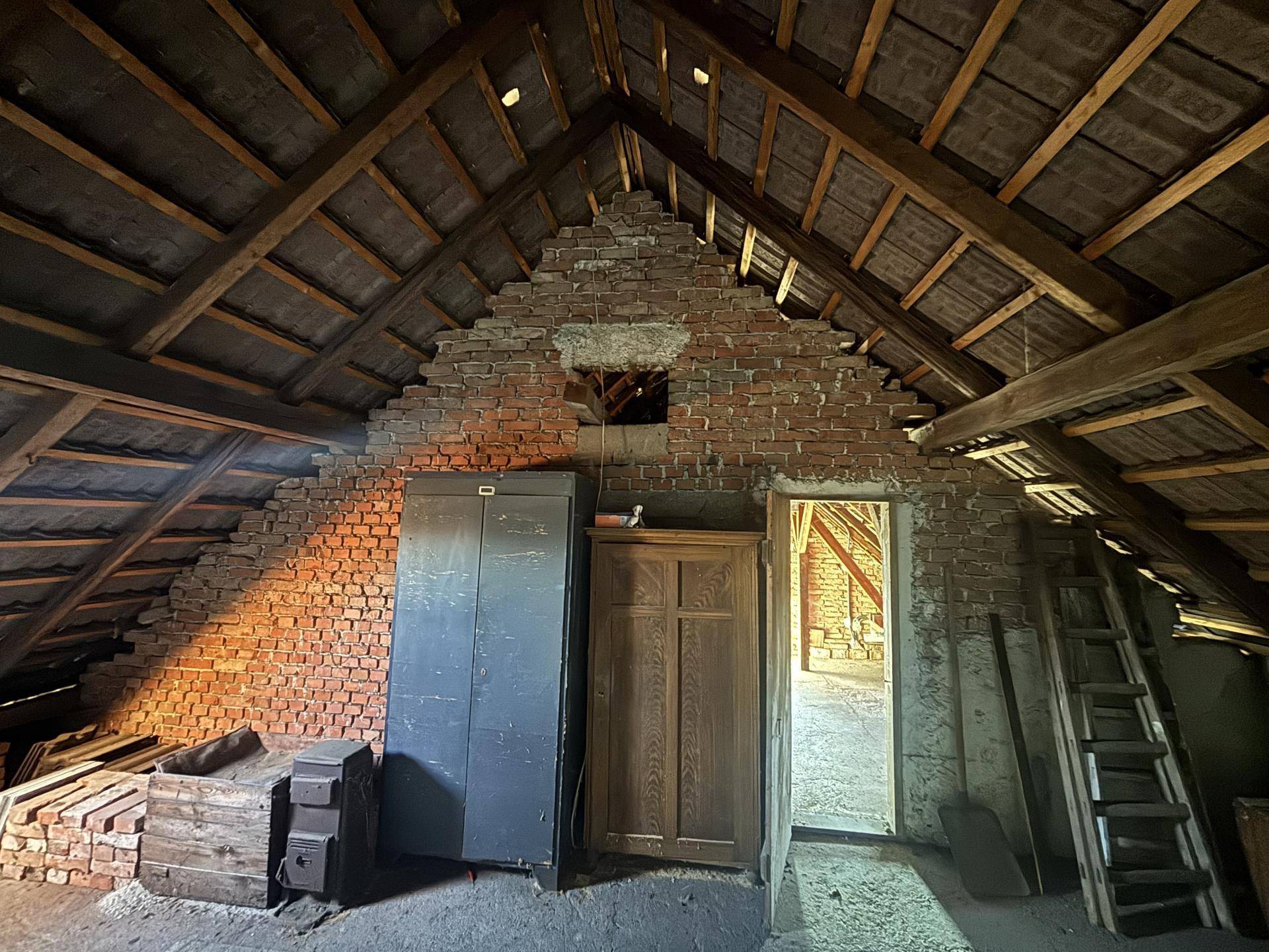 Geräumiger Dachboden mit freiliegenden Ziegelwänden und Holzbalken, ideal für Ausbau.